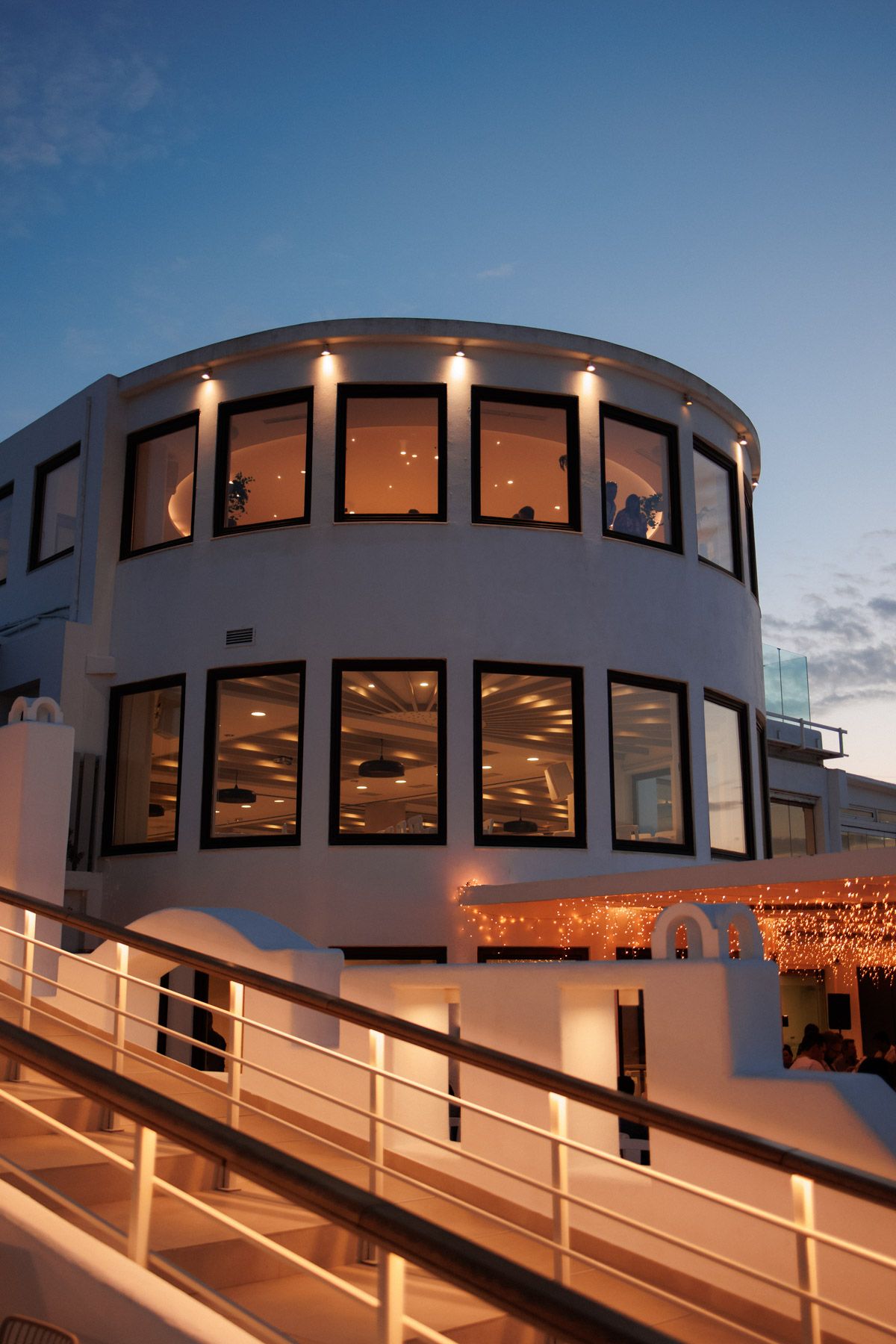 Elegant white circular wedding venue building illuminated at dusk in Santorini Greece.