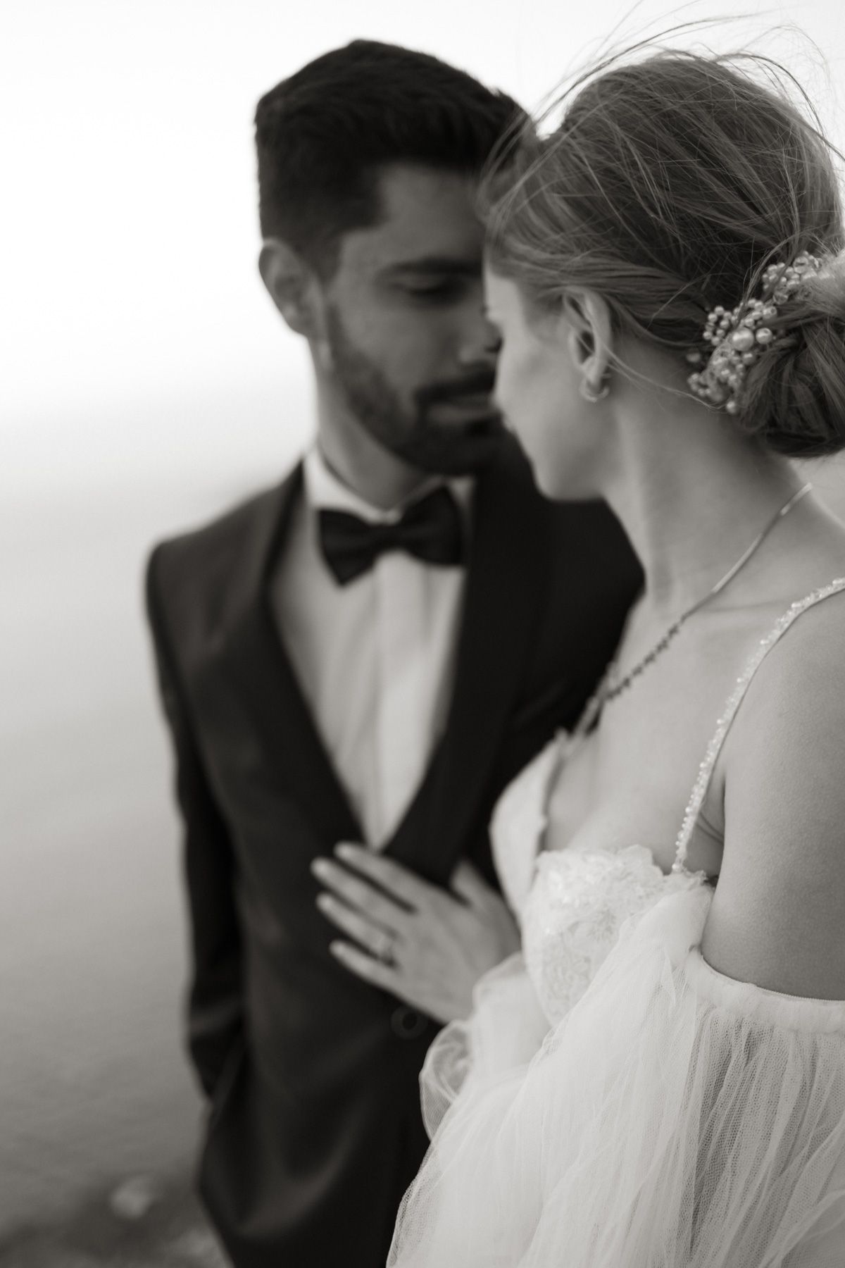 Black and white close-up of bride and groom in intimate moment, bride in lace gown, groom in tuxedo with bow tie.