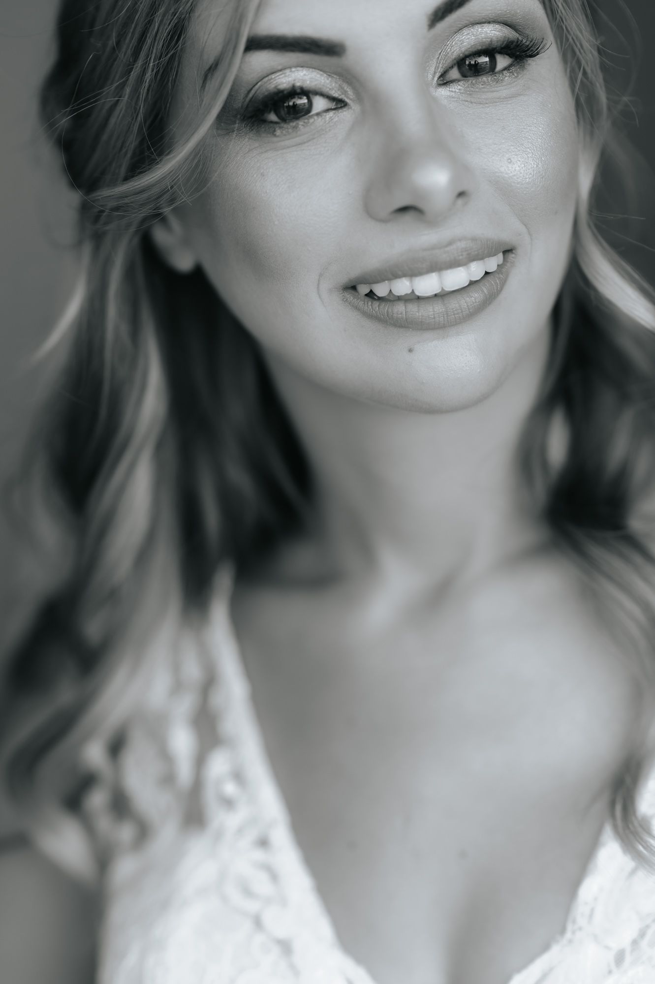 Elegant bride smiling in black and white portrait wearing lace wedding dress.