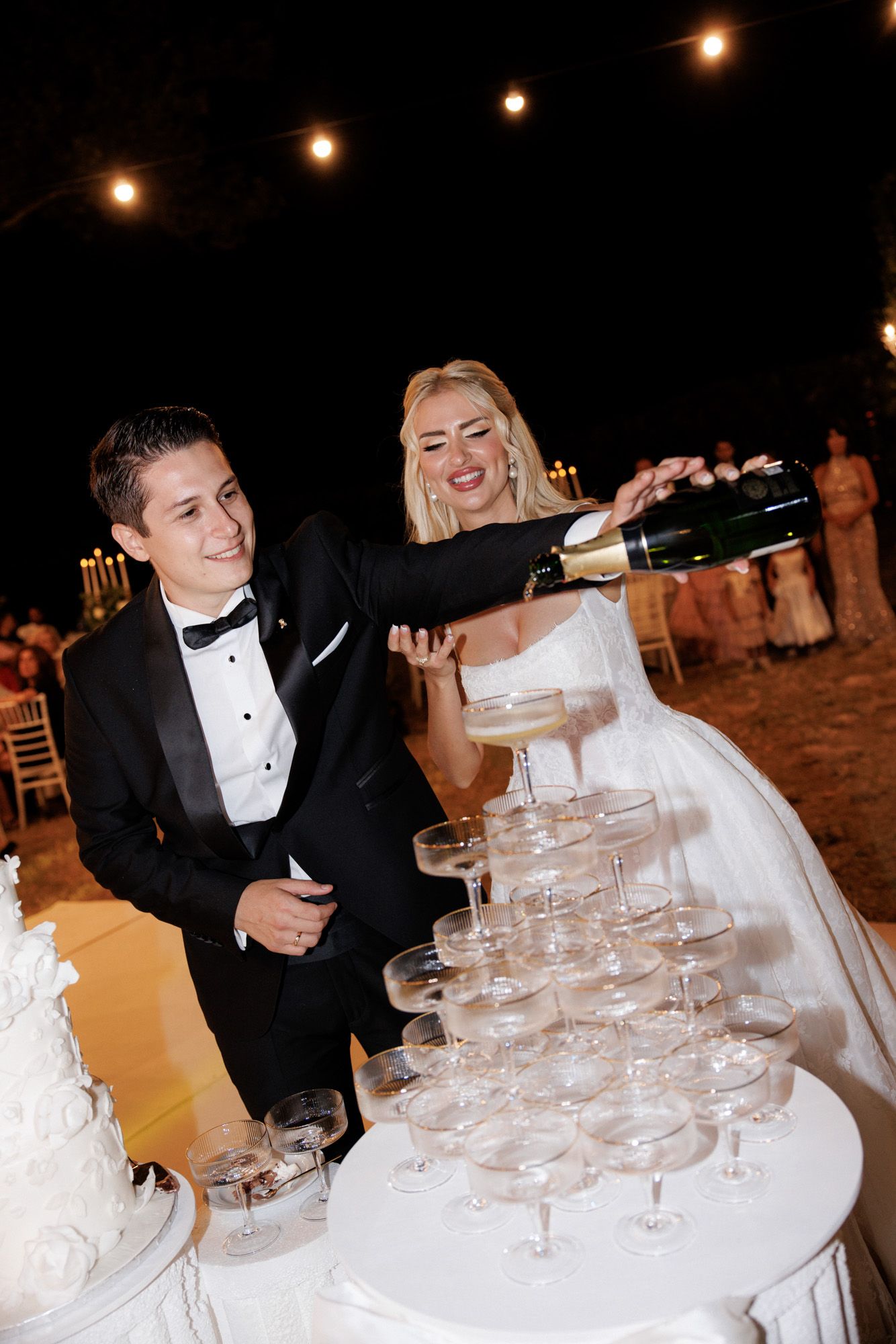 Bride and groom pouring champagne tower at elegant outdoor wedding reception.