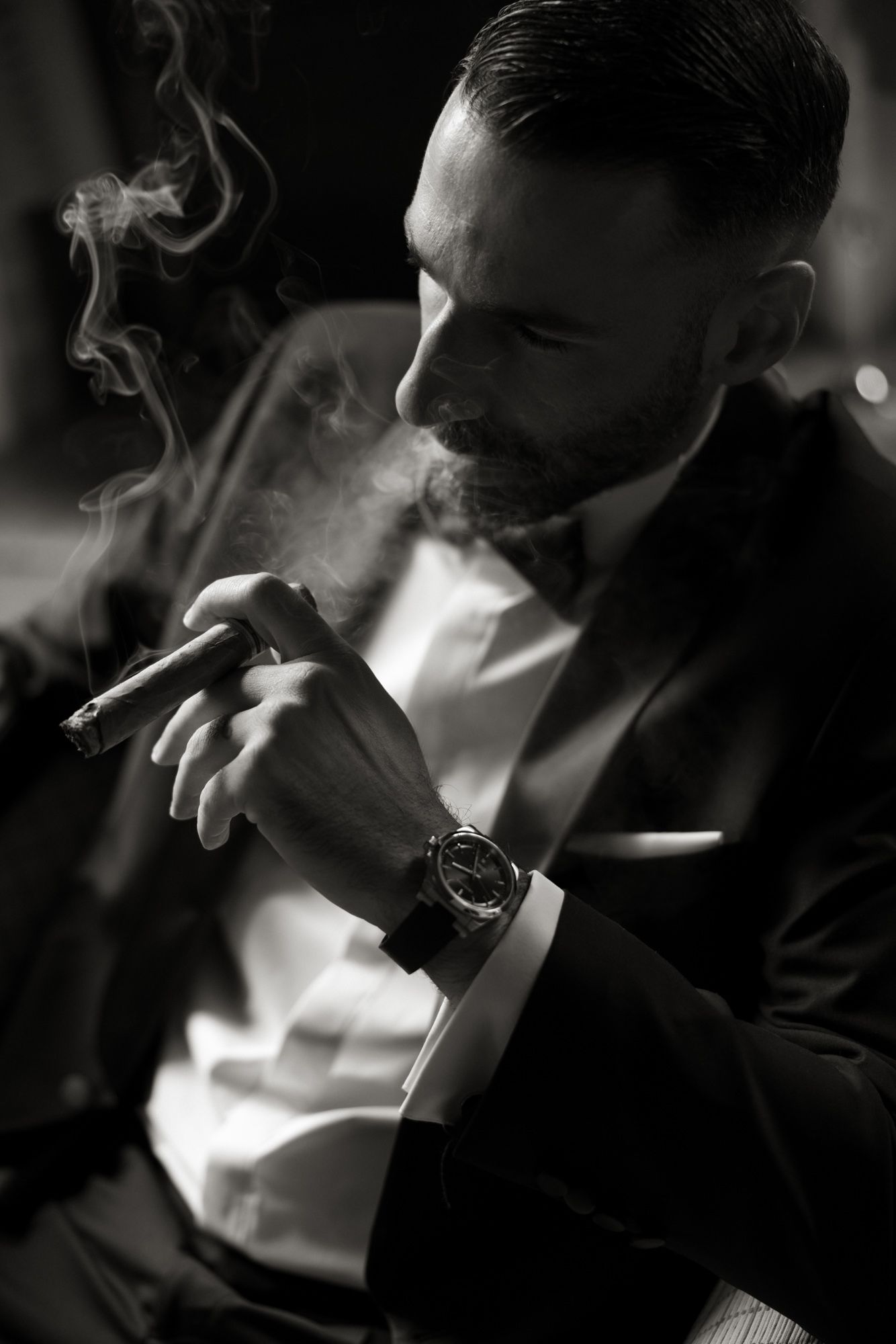 Elegant bearded man in black tuxedo smoking a cigar, black and white portrait photography.