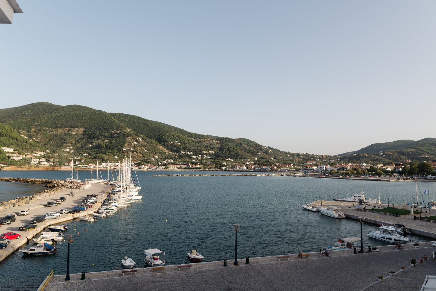 Scenic harbor view with sailboats and yachts docked against green hillside at dusk.