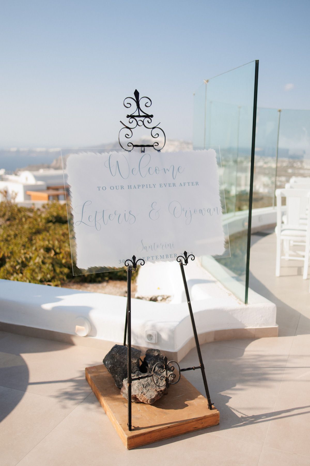 Elegant wedding welcome sign for Lefteris and Aryanna on decorative easel with Santorini backdrop.