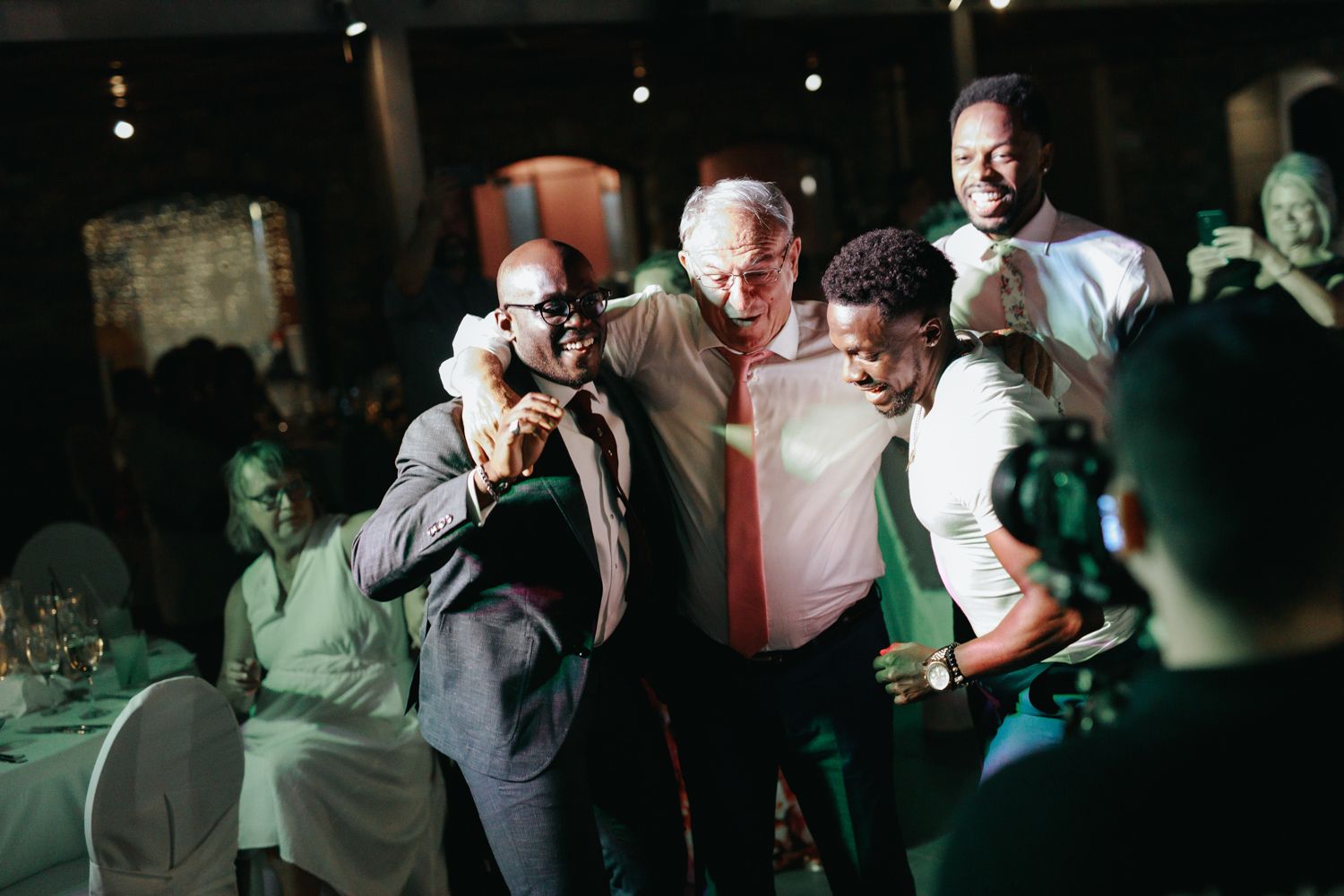 Group of men laughing and posing together at an indoor evening celebration or wedding reception.