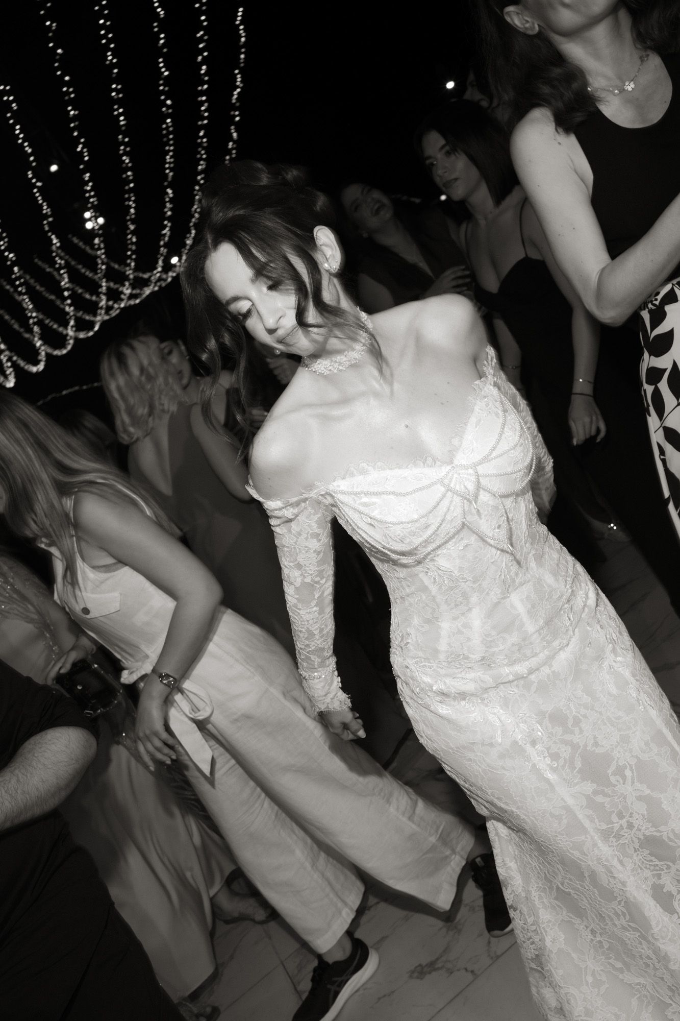 Bride in lace off-shoulder gown dancing with guests at elegant black and white wedding reception.