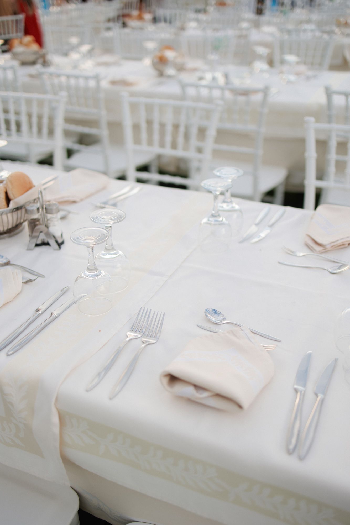 Elegant white wedding reception tables set with silver cutlery, crystal glasses, and folded linen napkins.