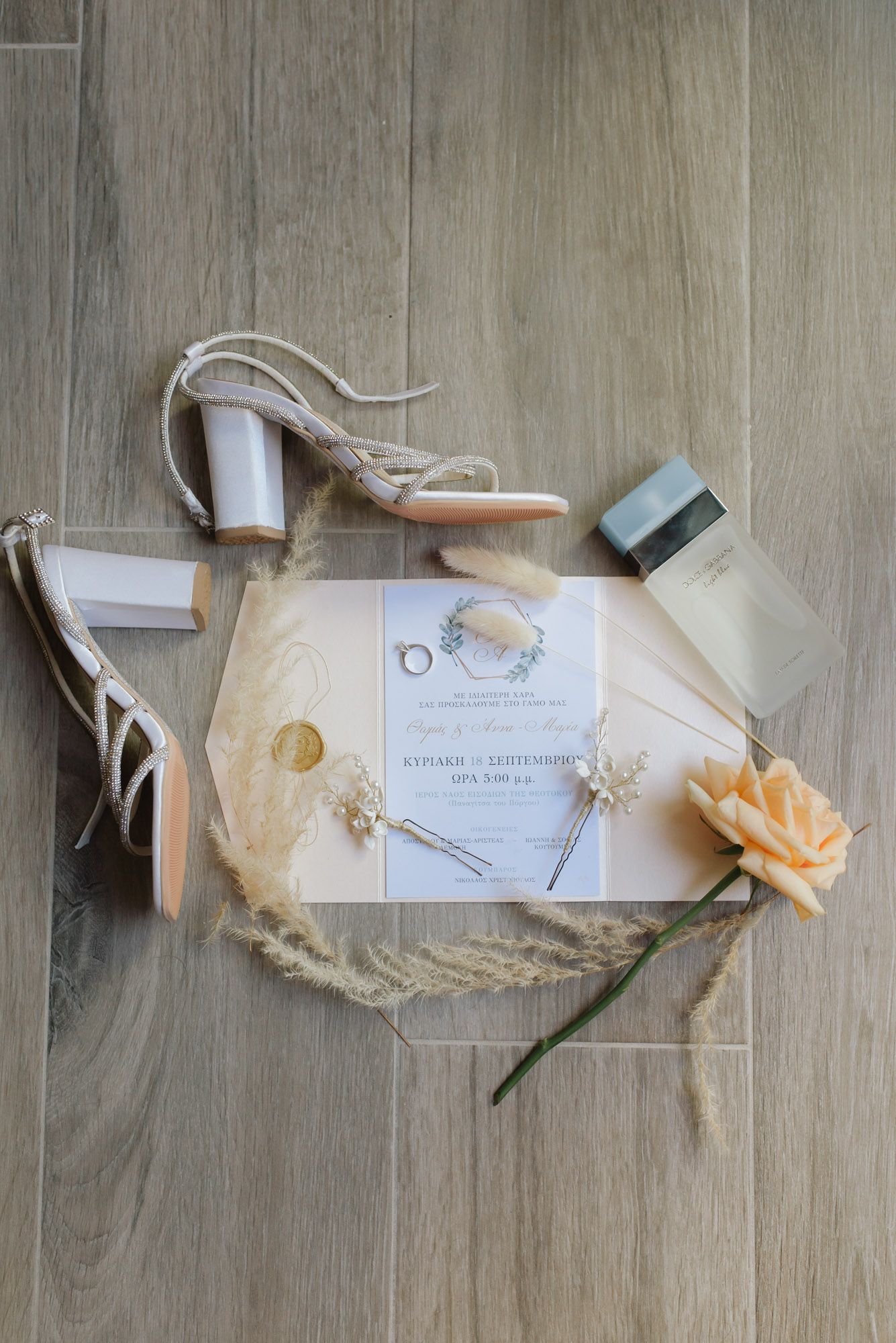 Boho wedding flat lay with invitation, heels, rings, perfume, and dried pampas grass.