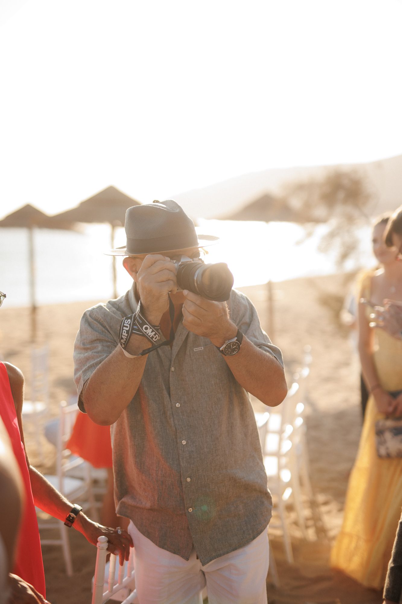 Photographer capturing moments at golden hour beach wedding ceremony with guests.