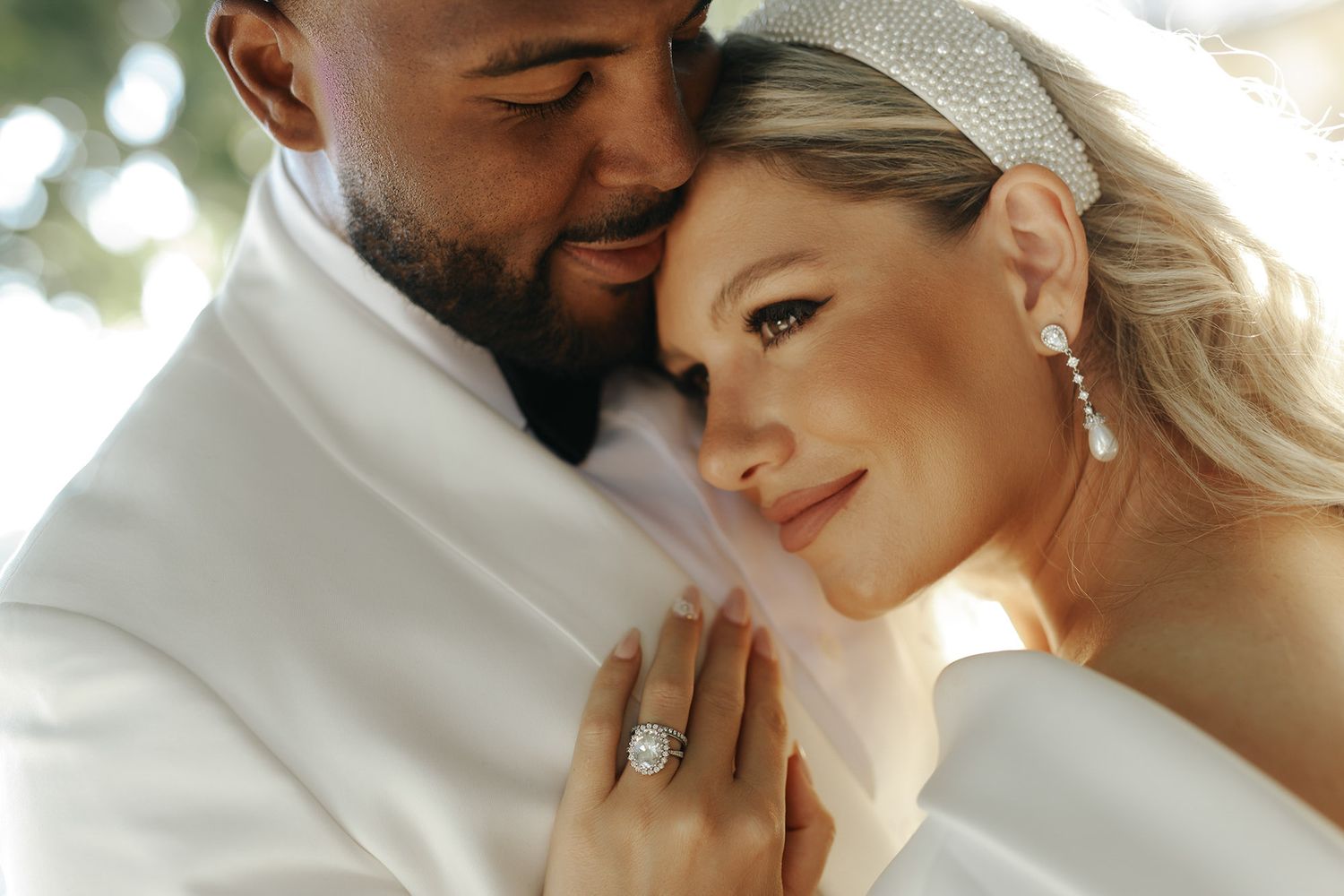 Close up romantic moment of happy newlyweds in white wedding attire smiling and embracing outdoors.