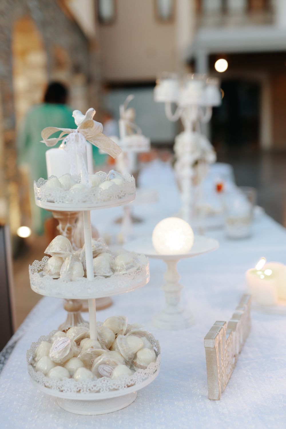 Elegant white tiered dessert stand with chocolate truffles and candles on a white tablecloth at a wedding reception.