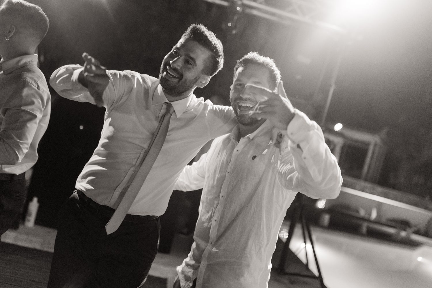 Two men in dress shirts celebrate together at an event, one covering his eyes, in black and white photo.