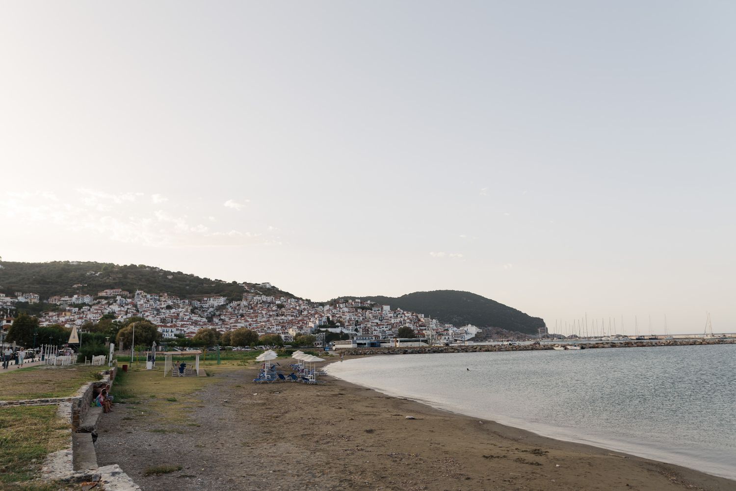 Panoramic view of a Greek coastal town with white buildings nestled against a hill at dusk.