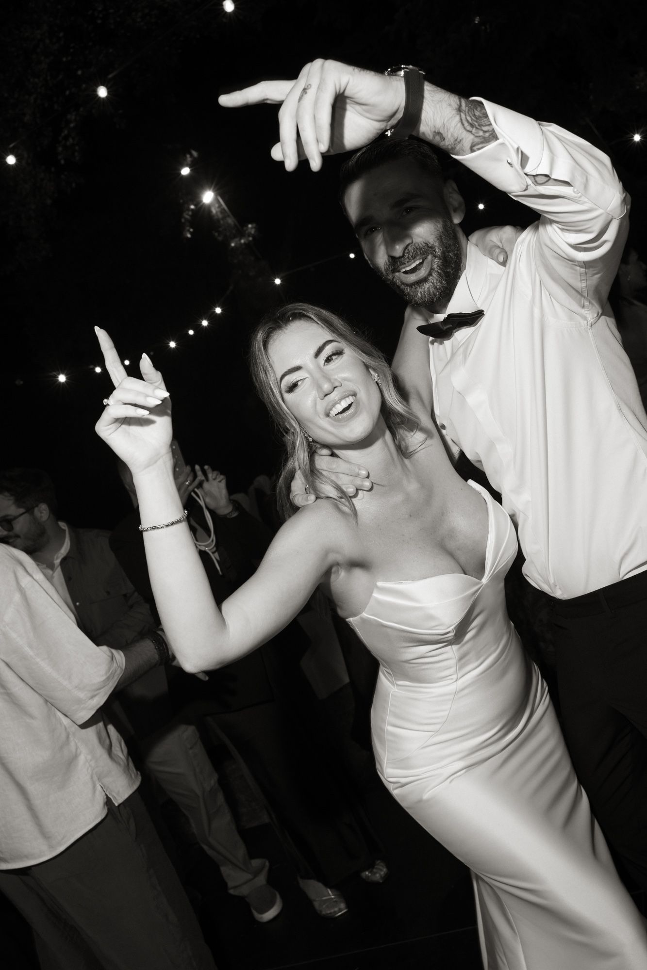 Black and white photo of a bride and groom dancing joyfully at their wedding reception.