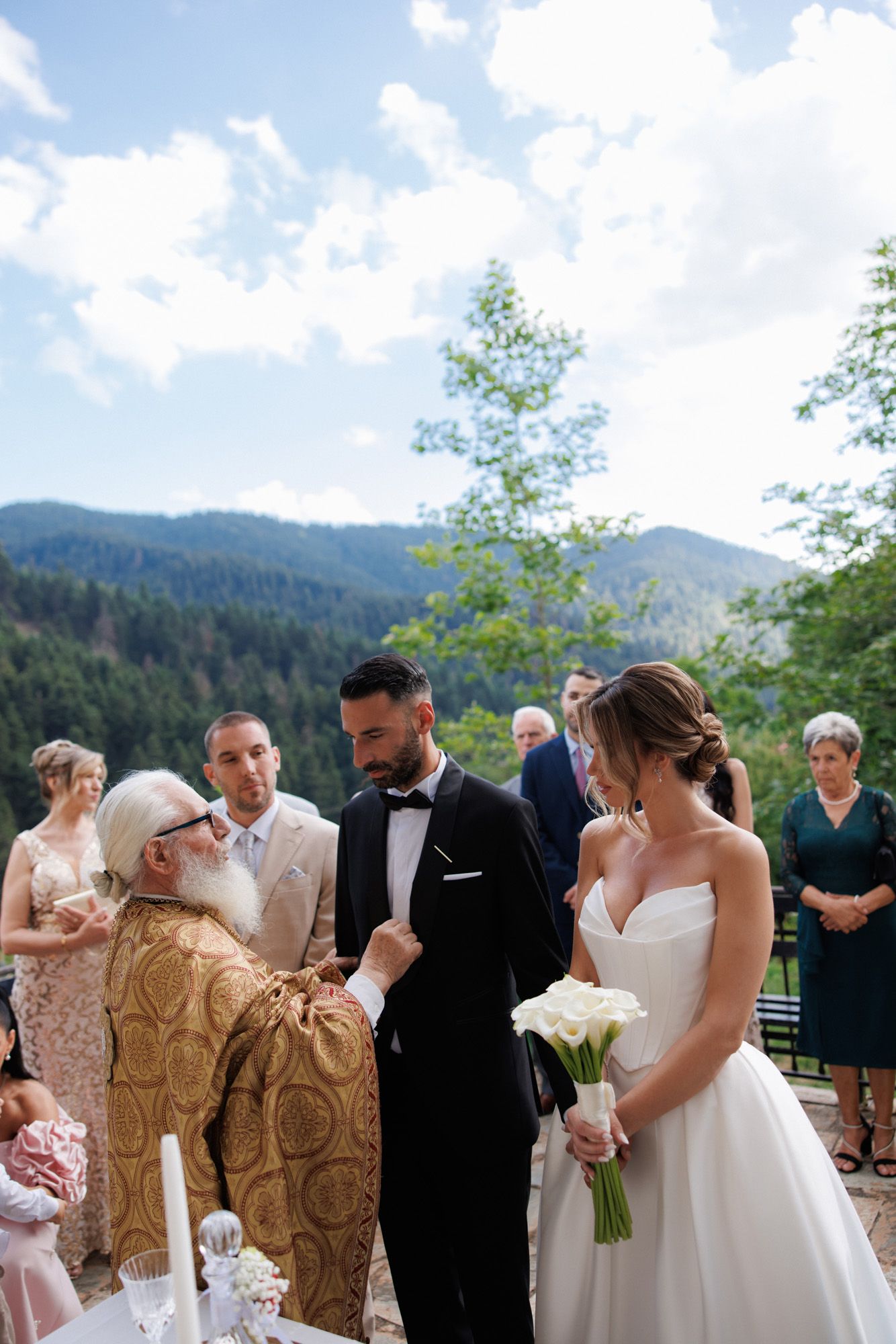 Orthodox priest performing outdoor wedding ceremony with couple in mountain landscape setting.