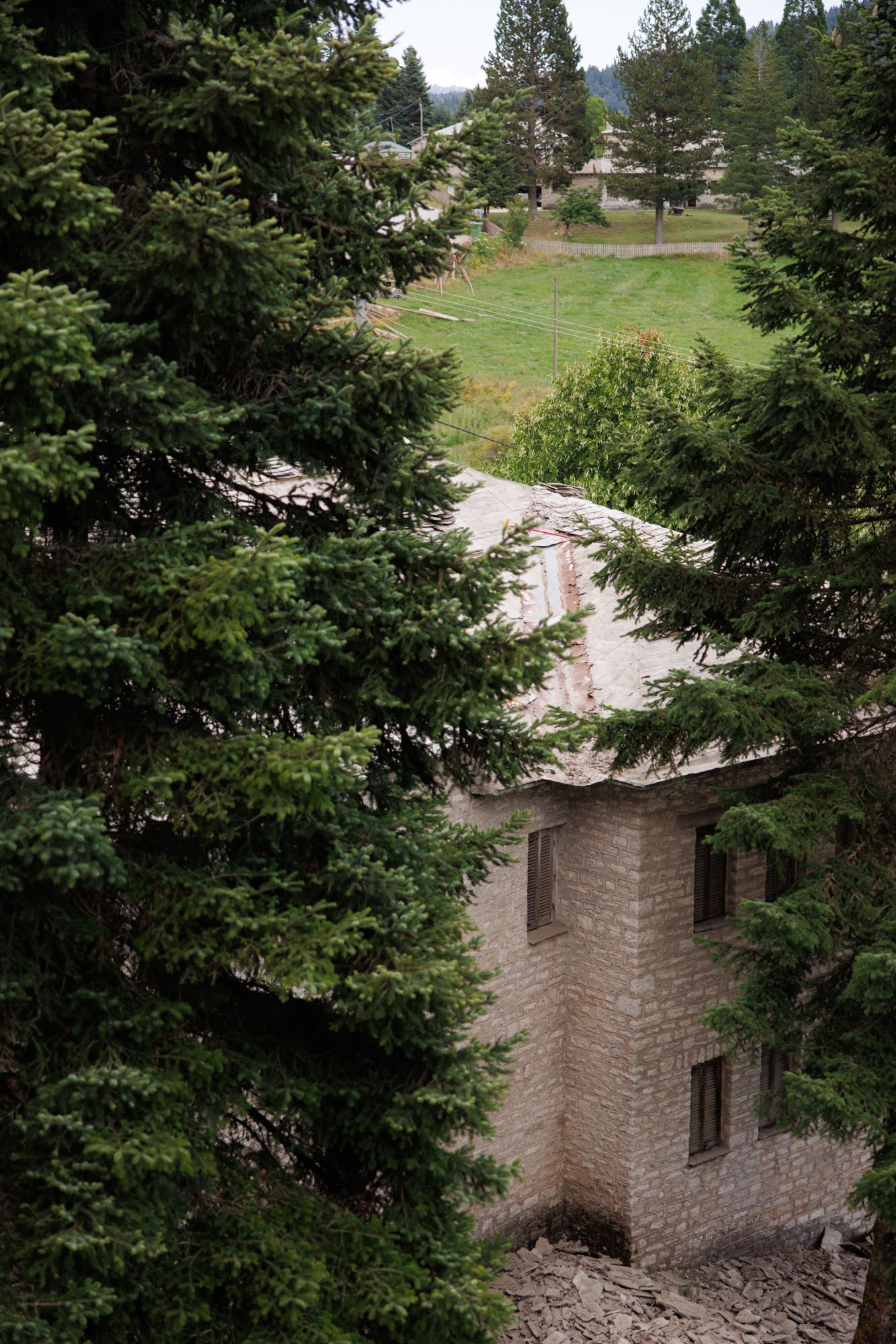 Aerial view of a stone building surrounded by tall pine trees in a mountain landscape.