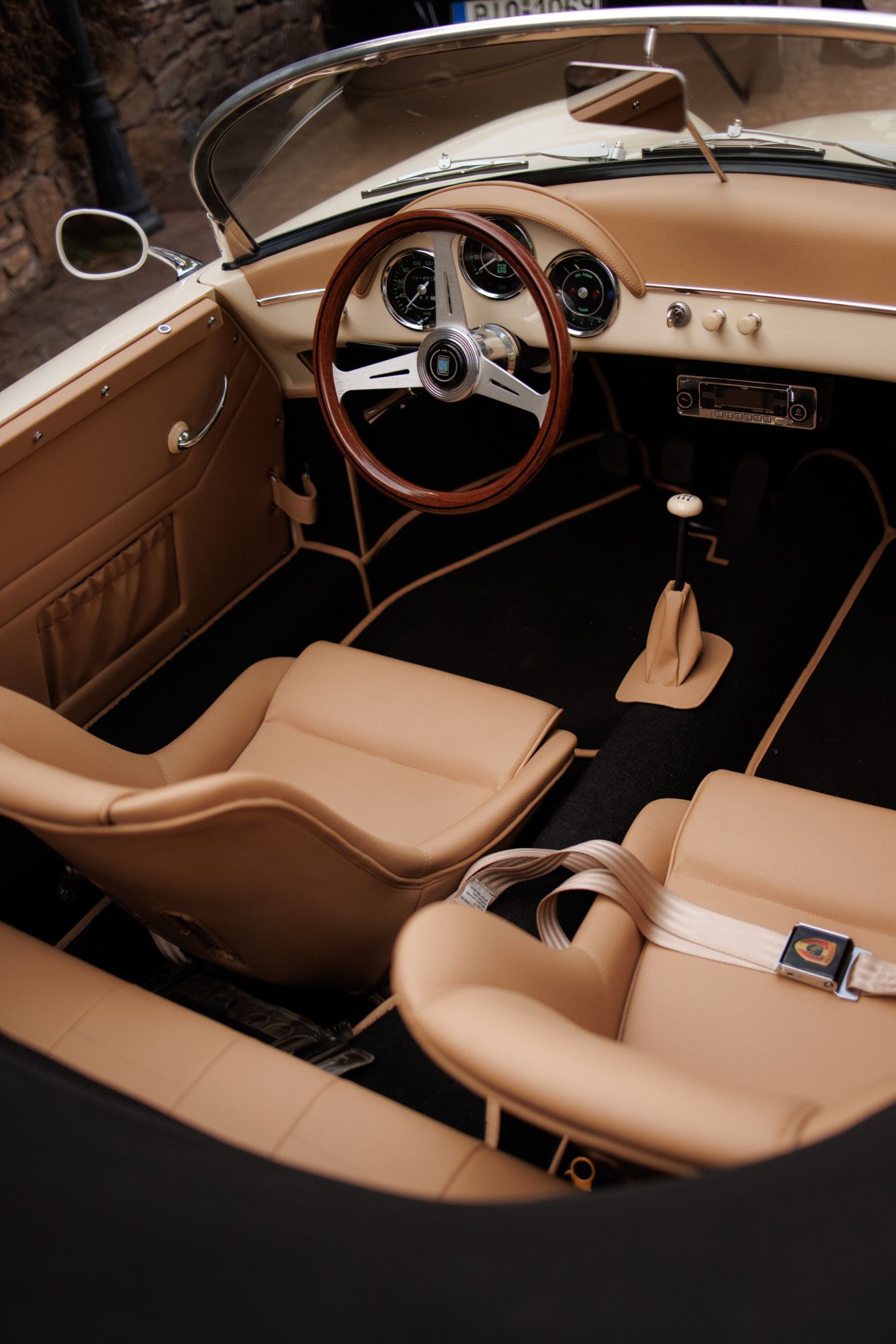 Luxurious tan leather interior of a vintage Porsche 356 with wooden steering wheel and classic dashboard.