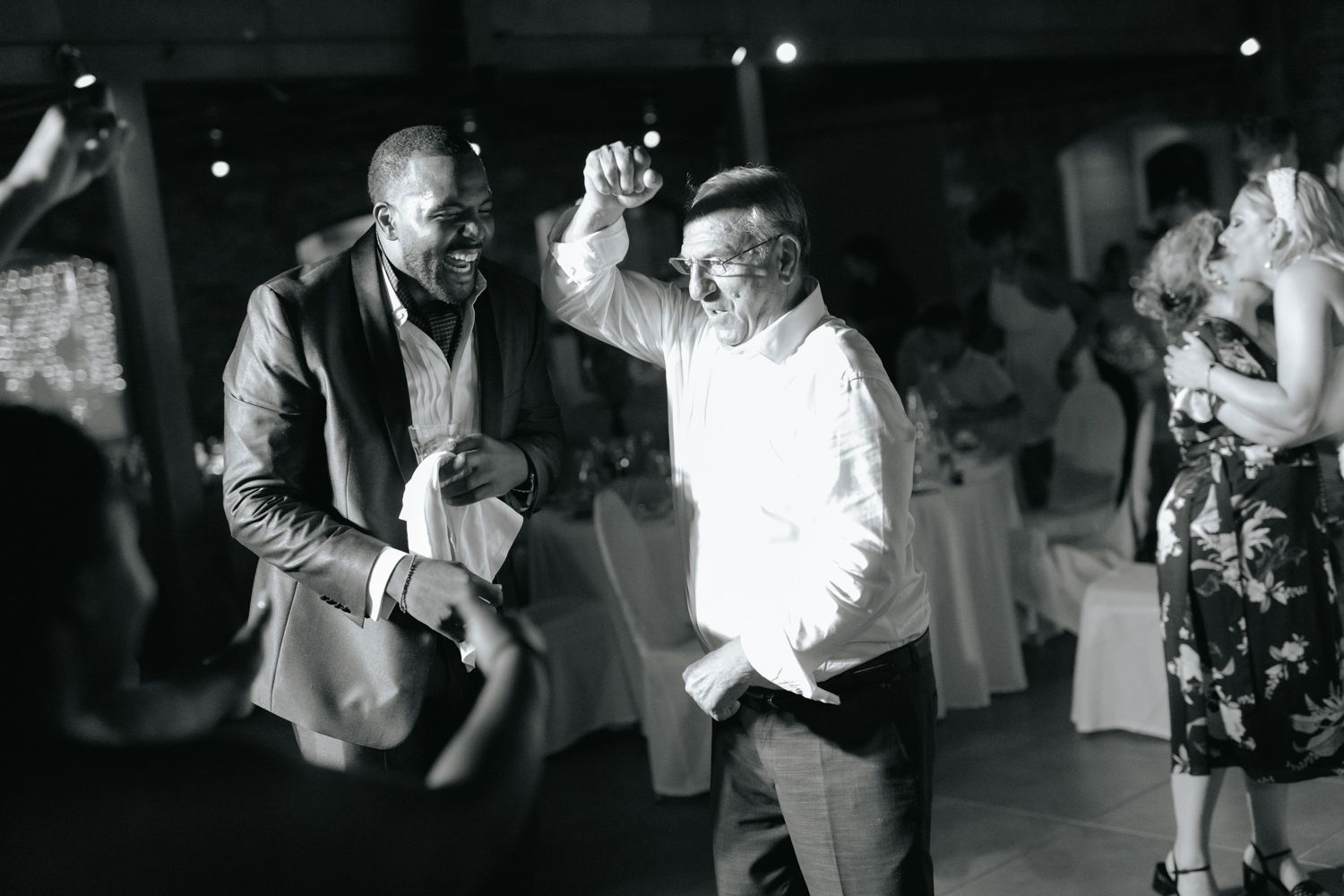 Two men dancing joyfully at a wedding reception in black and white photo.
