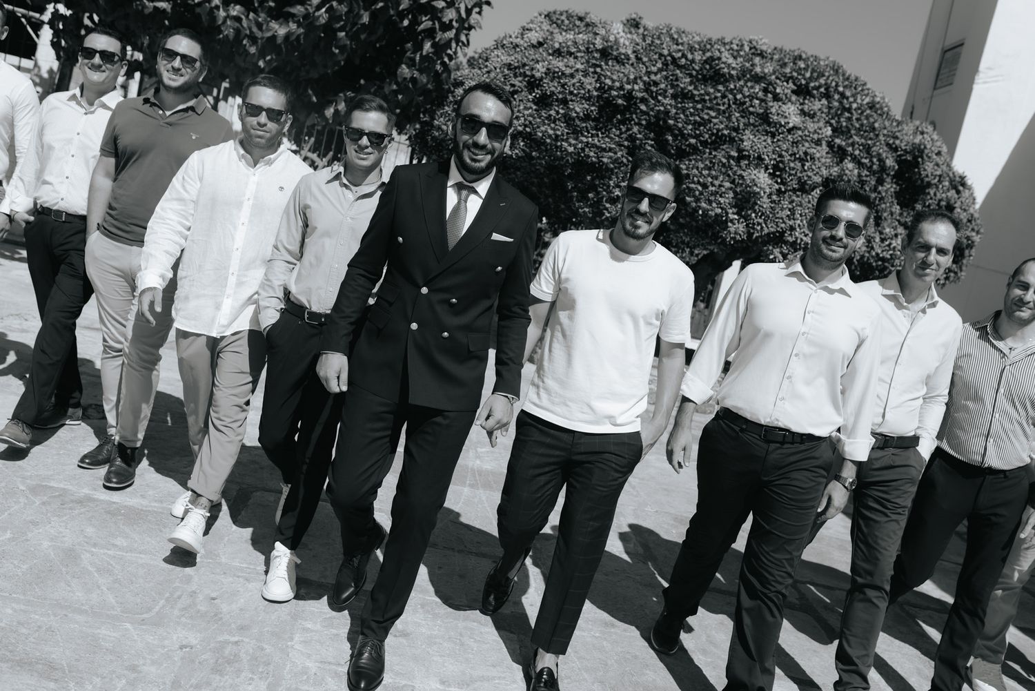 Black and white photo of groom and groomsmen walking confidently together in stylish wedding attire.