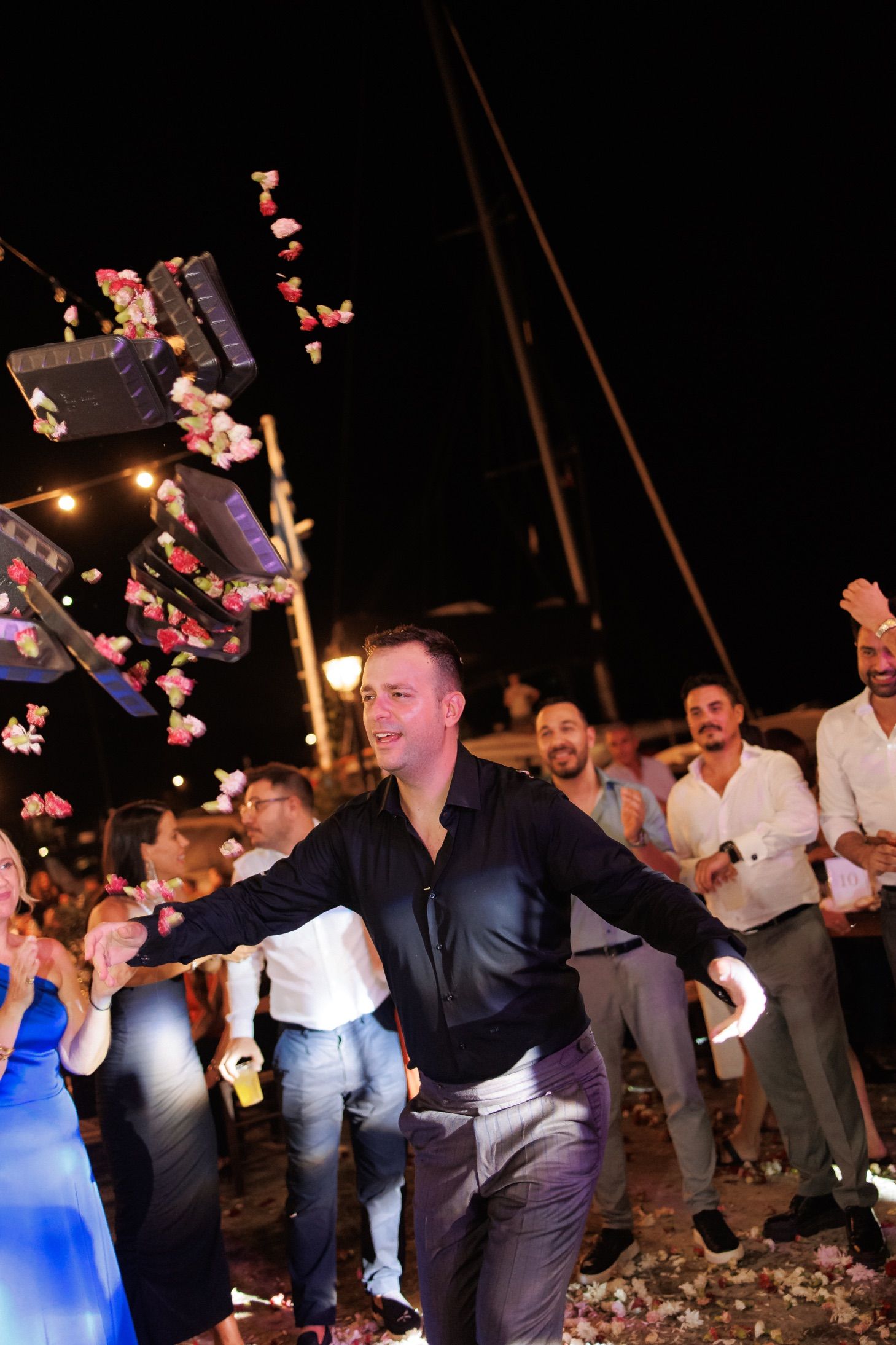 Groom dancing joyfully with arms outstretched as flower petals rain down at wedding.