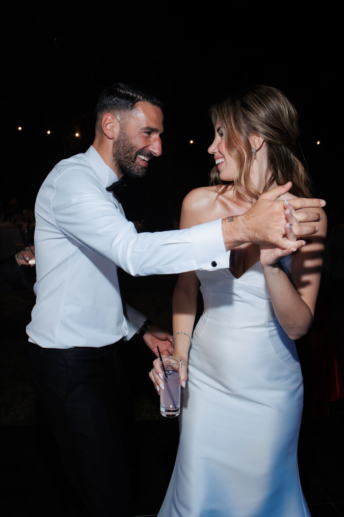 Bride and groom laughing together while dancing at outdoor evening wedding reception celebration.