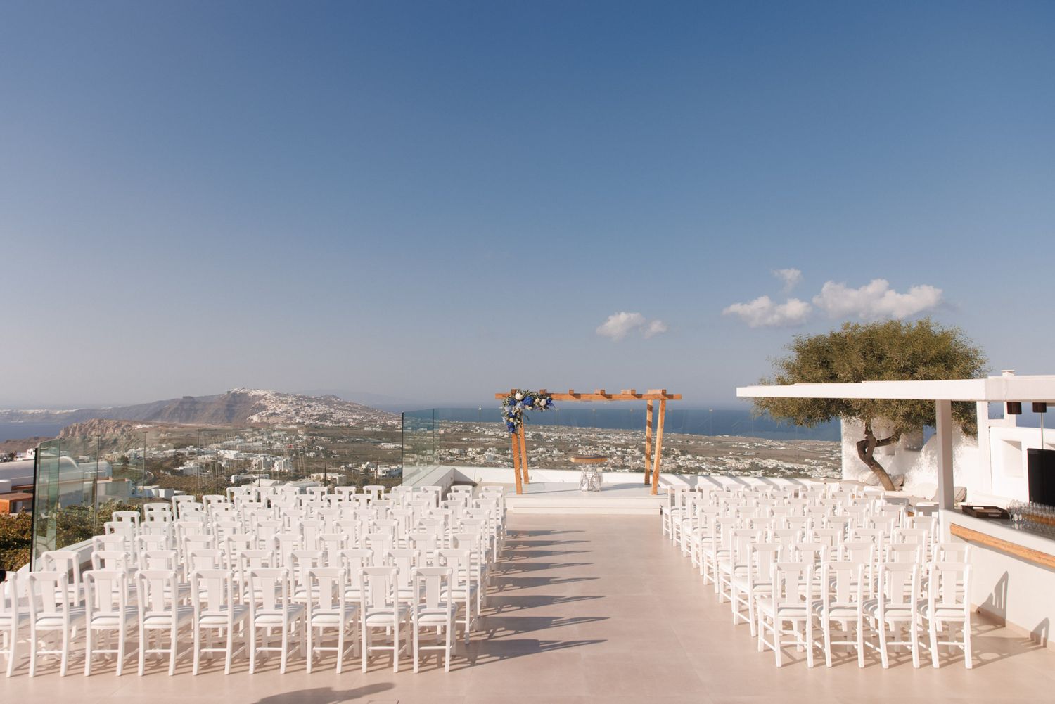 Outdoor wedding ceremony venue in Santorini with white chairs and panoramic sea view.