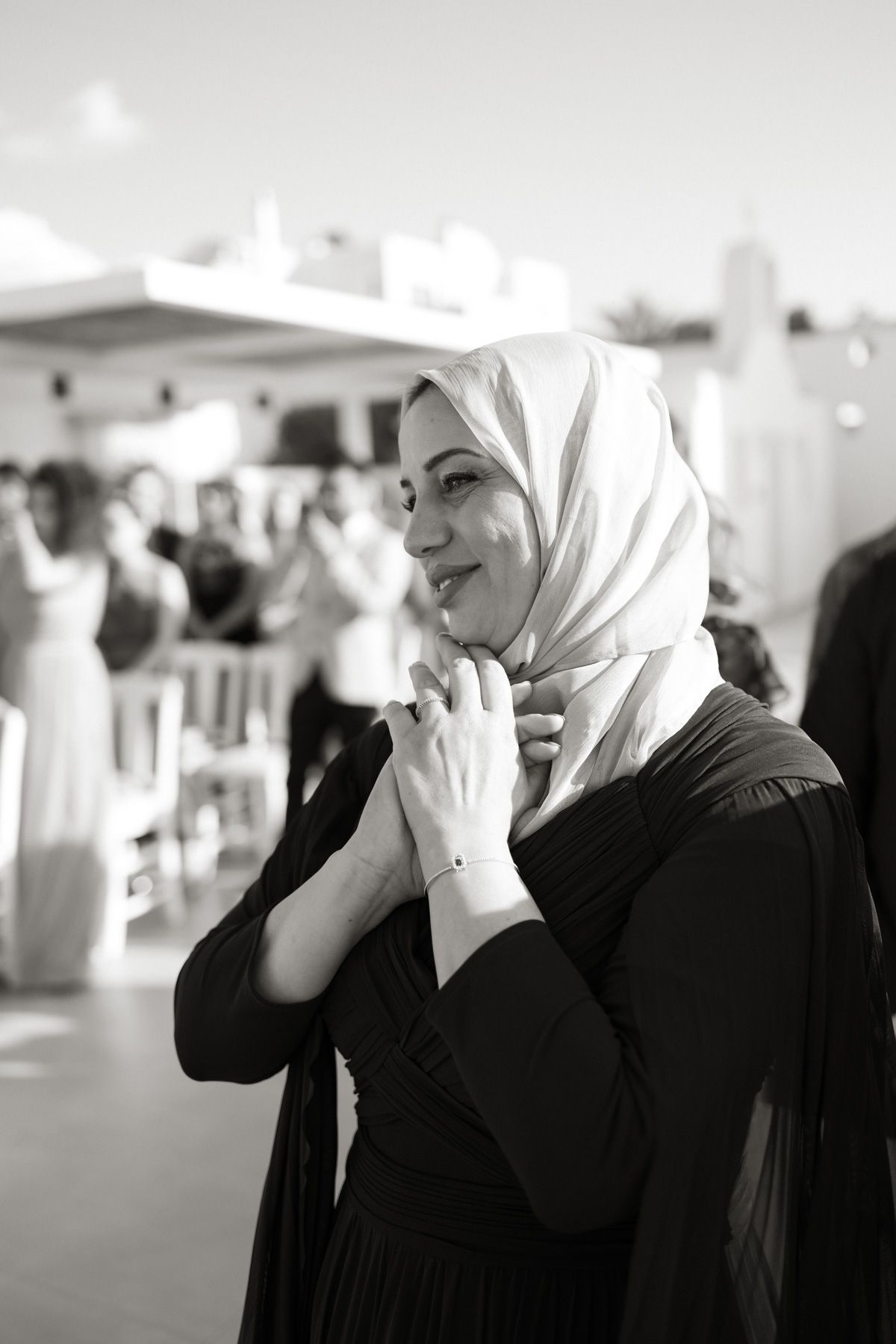 Black and white portrait of a smiling woman in hijab at an outdoor wedding celebration.
