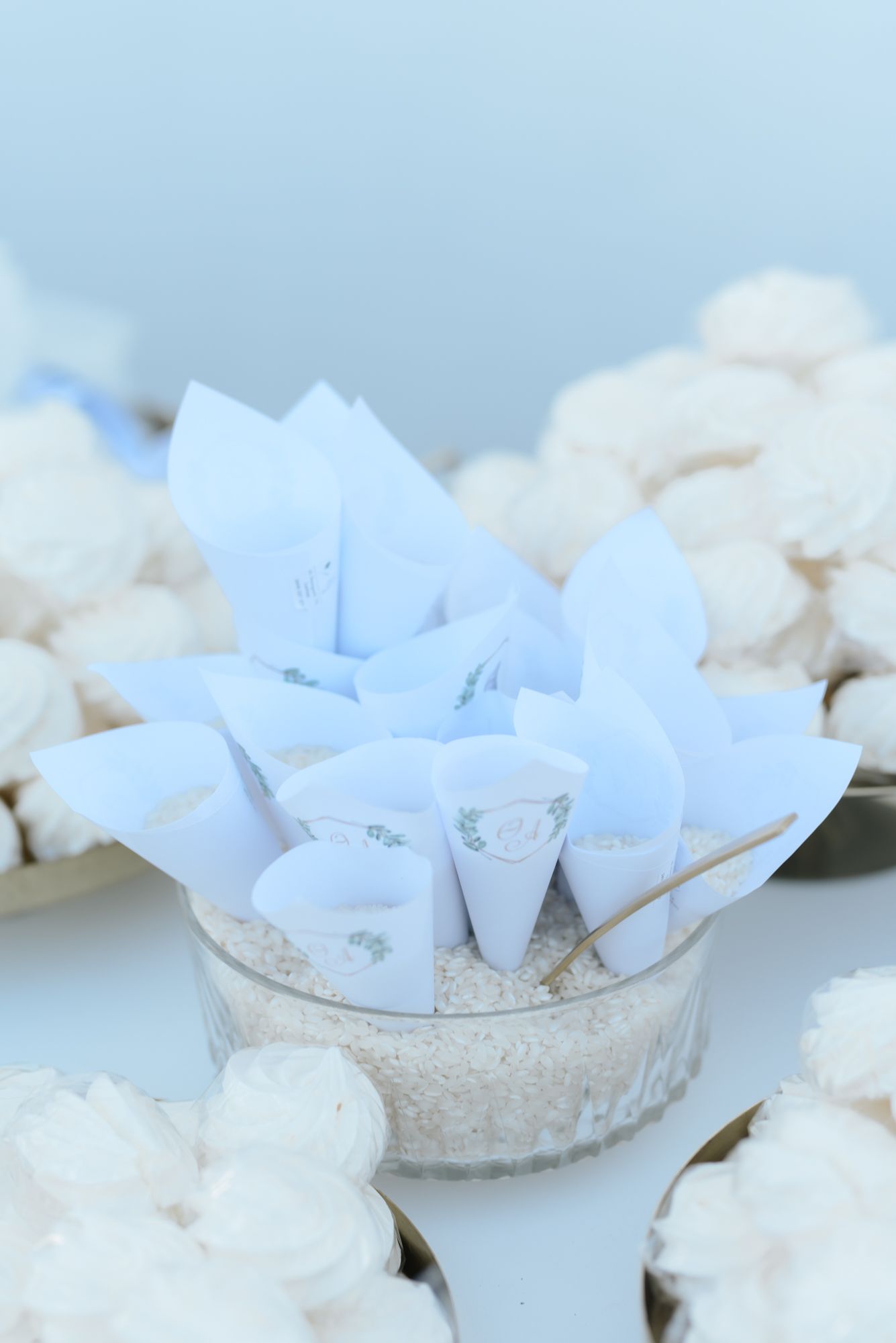 White paper cone wedding favors displayed in glass bowl surrounded by white flowers.