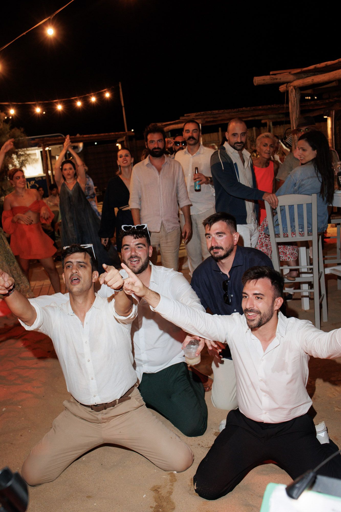 Group of men celebrating on knees at an outdoor nighttime wedding party in Greece.