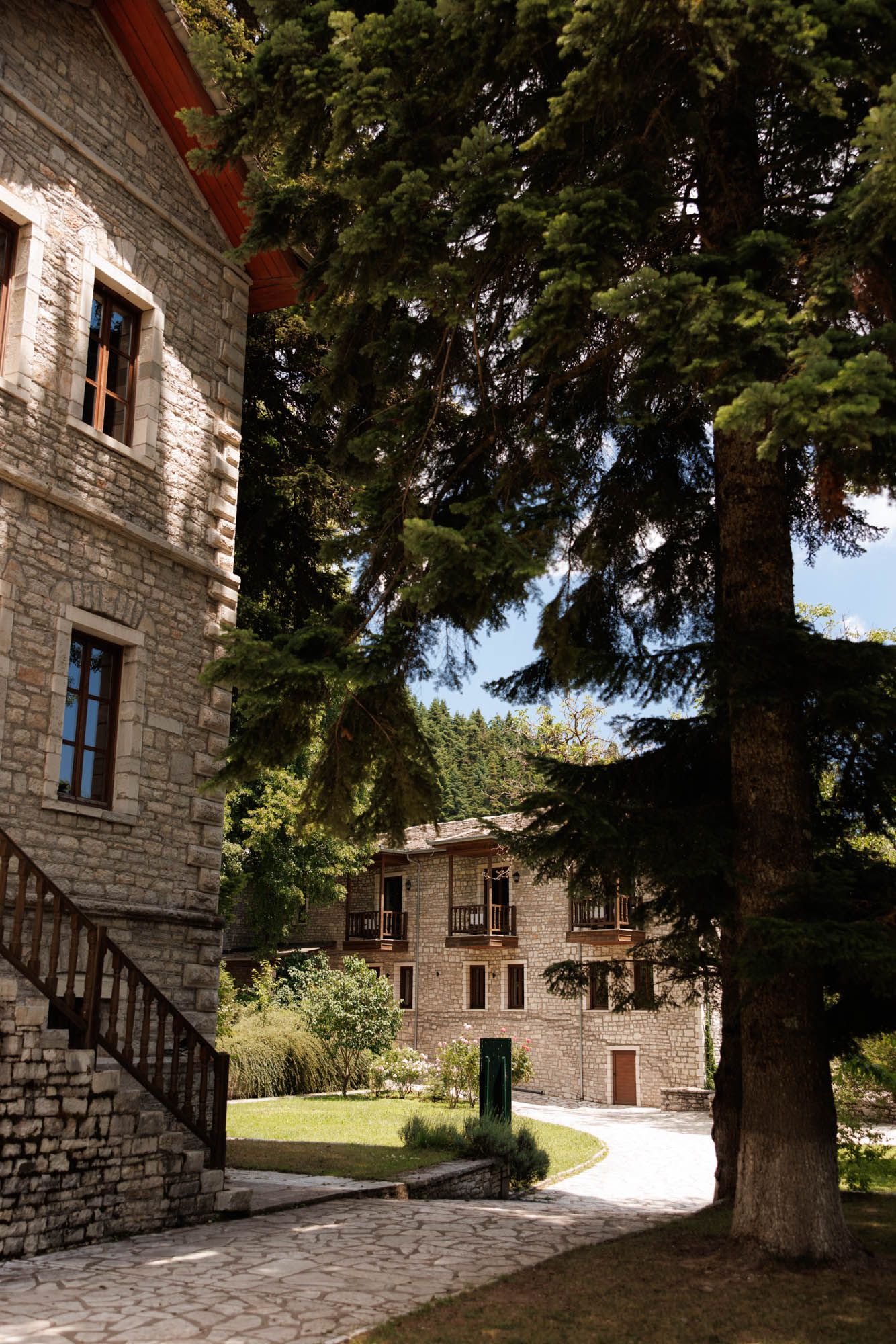 Stone wedding venue with exterior staircase and tall pine trees in lush garden setting.