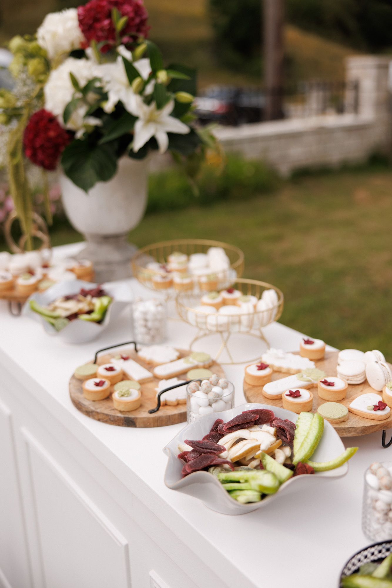 Elegant outdoor wedding dessert table with macarons, pastries, and fresh floral arrangements.