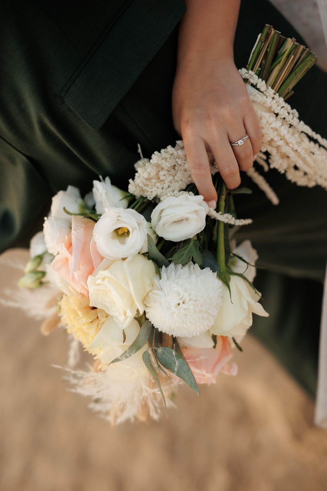 Close-up of bridal bouquet with white dahlias, pink roses, and diamond engagement ring.
