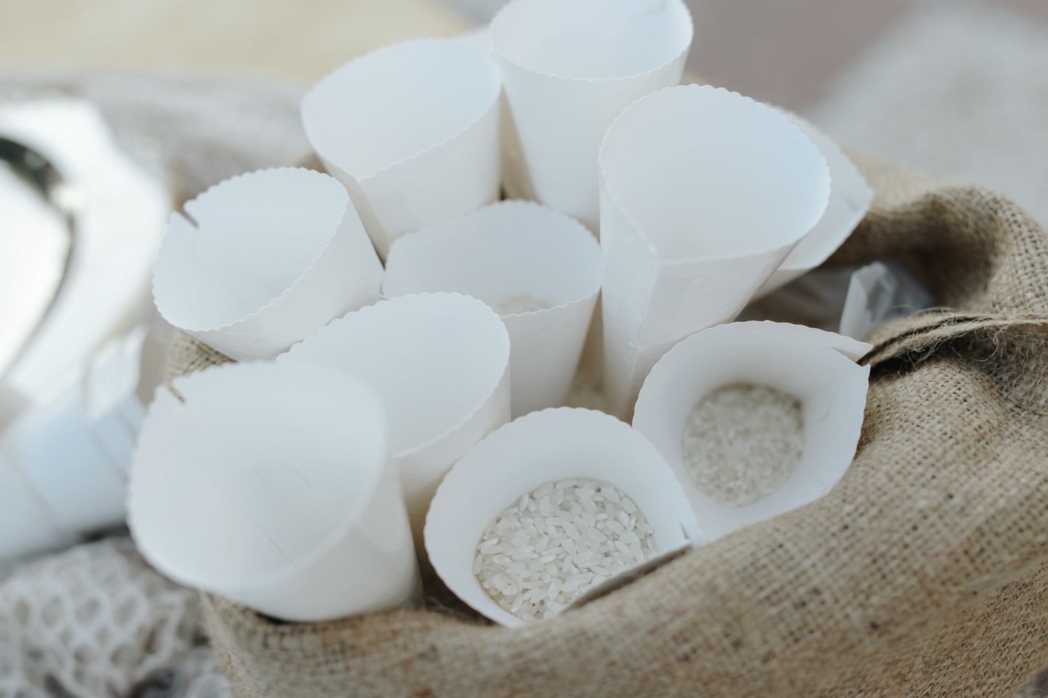 White paper cone cups filled with rice displayed on burlap fabric for a wedding ceremony.
