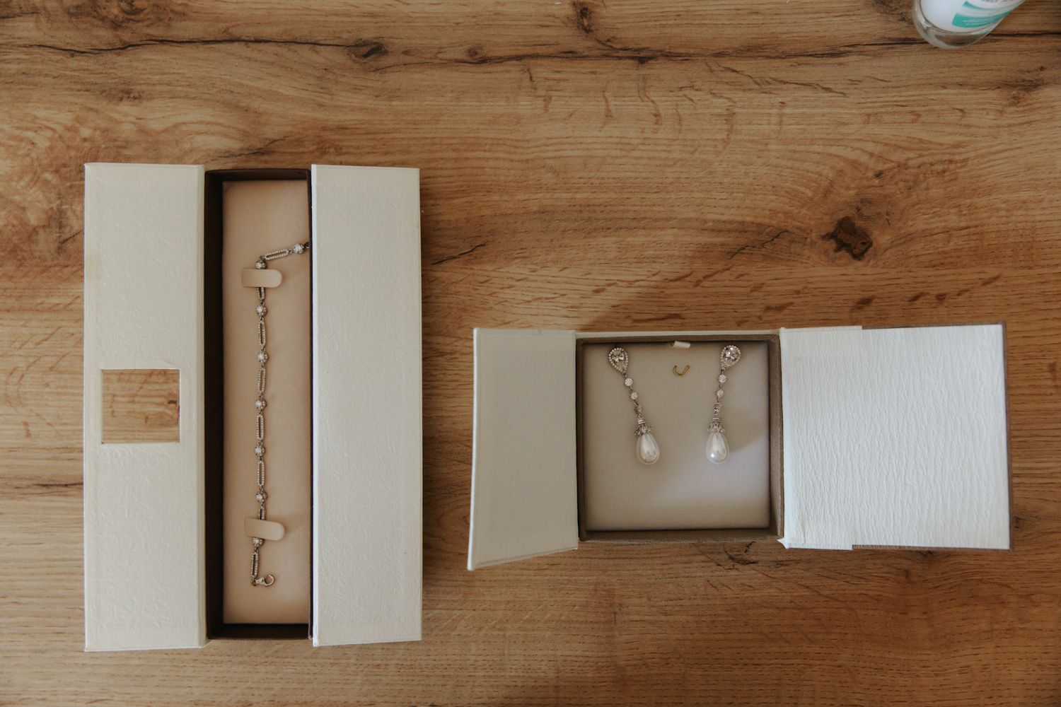 Two open jewelry gift boxes on wood surface displaying a delicate bracelet and pearl drop earrings with silver settings.