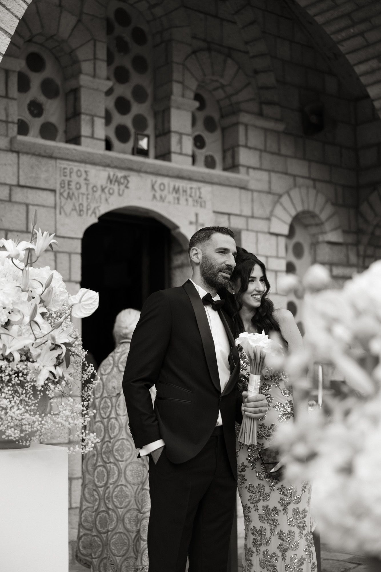 Black and white photo of bride and groom standing outside an Orthodox church after ceremony.