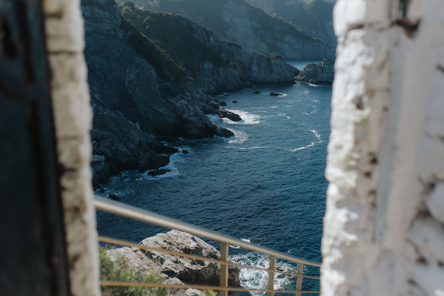 Dramatic coastal cliffs and deep blue sea viewed through a rustic stone window frame opening.