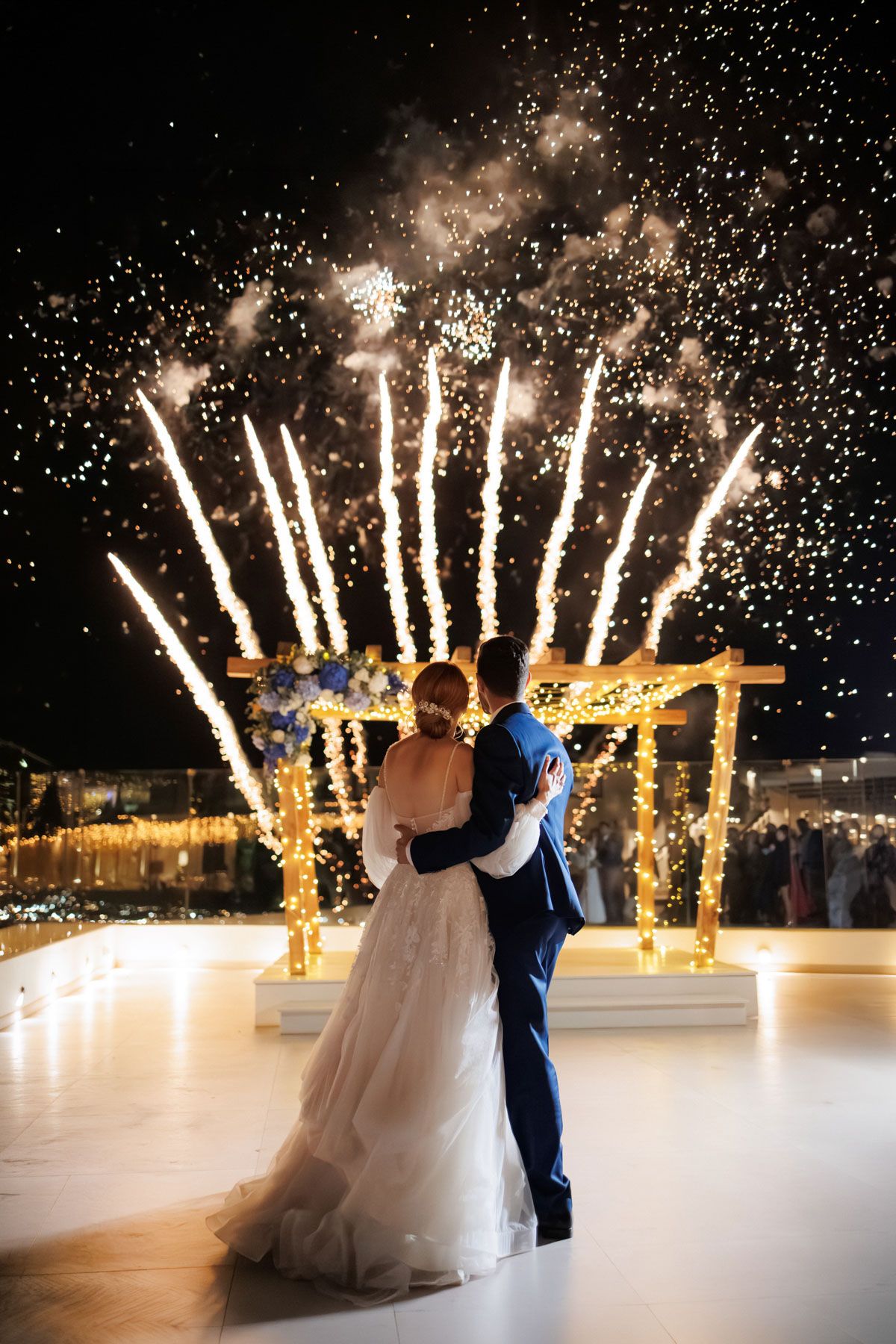 Bride and groom embrace as spectacular fireworks display lights up the sky at wedding reception.