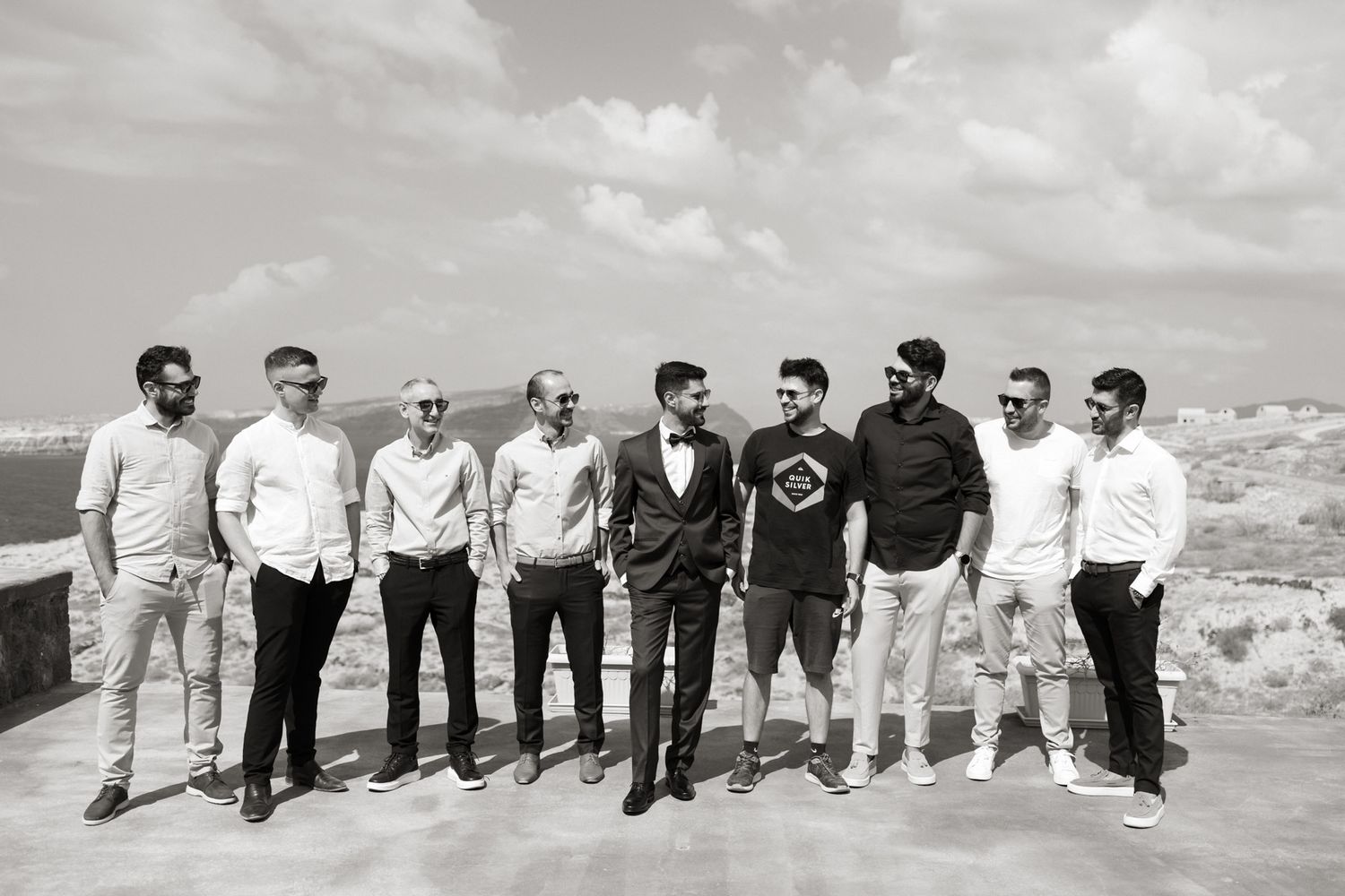 Groom with groomsmen posing outdoors on a rooftop terrace in black and white photo.