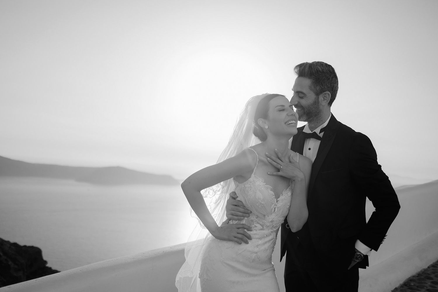 Romantic black and white wedding couple embracing at sunset overlooking the Santorini caldera.