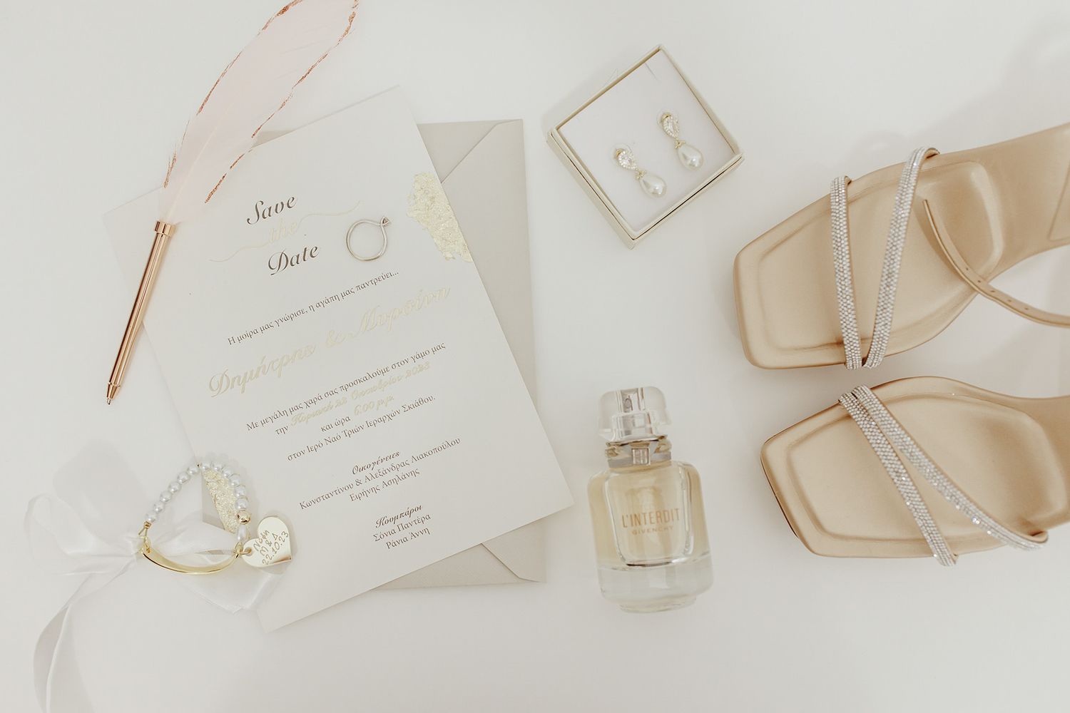 Wedding details flatlay with invitation card, perfume bottle, and elegant beige sandals on white background.