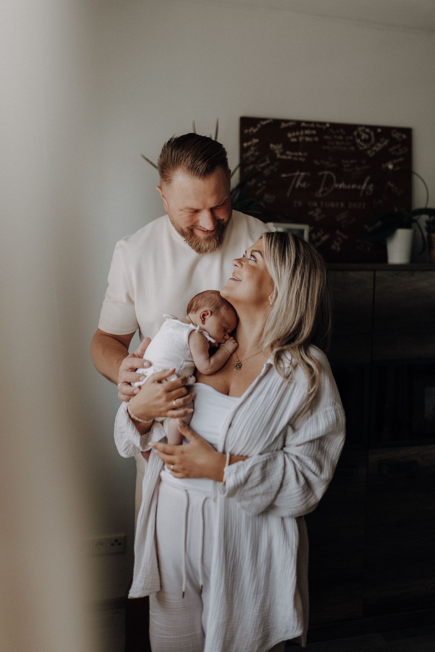 Smiling parents holding their newborn baby together in a warm and intimate home setting.