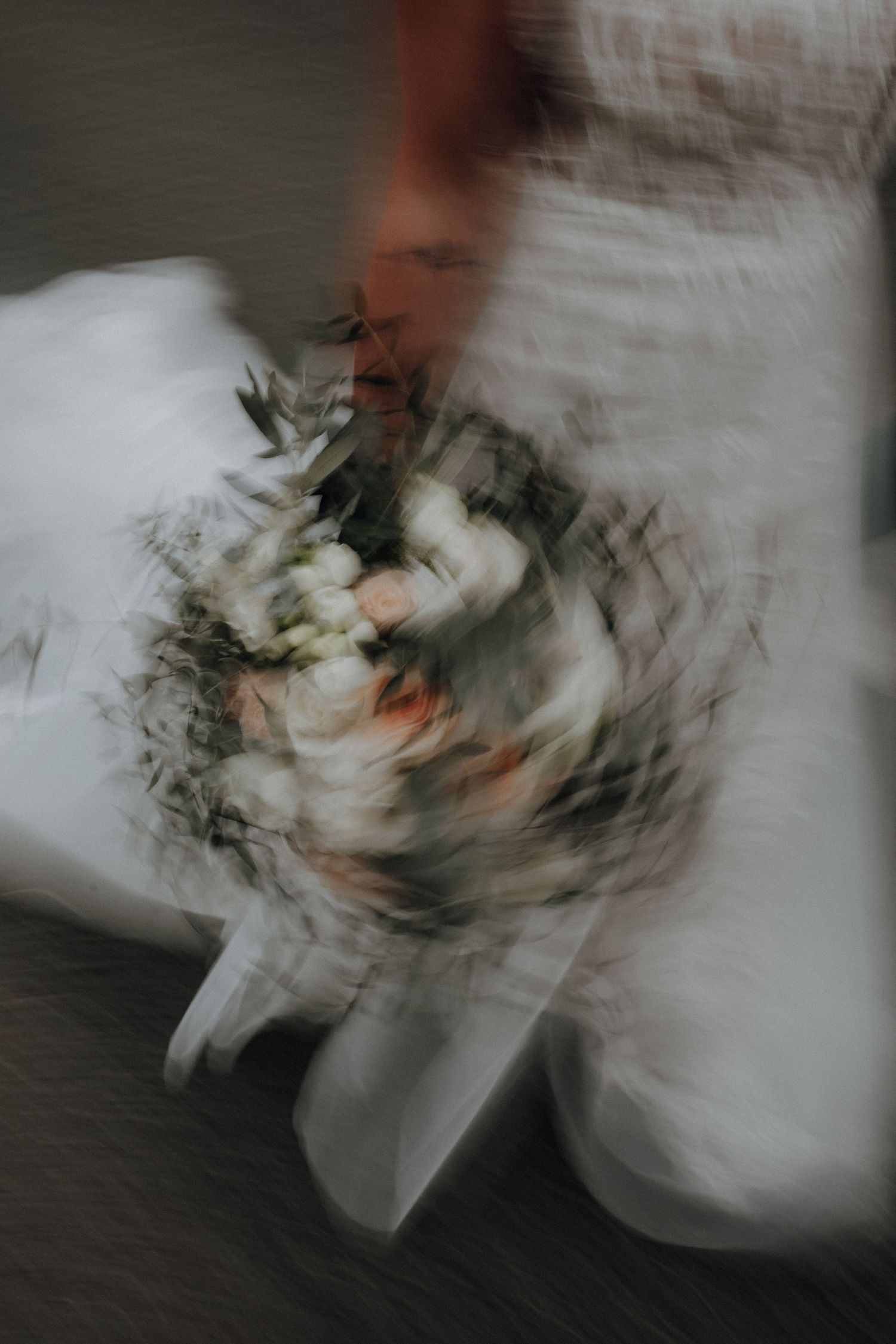Artistic motion blur photo of bride holding a floral bouquet in a white wedding dress.