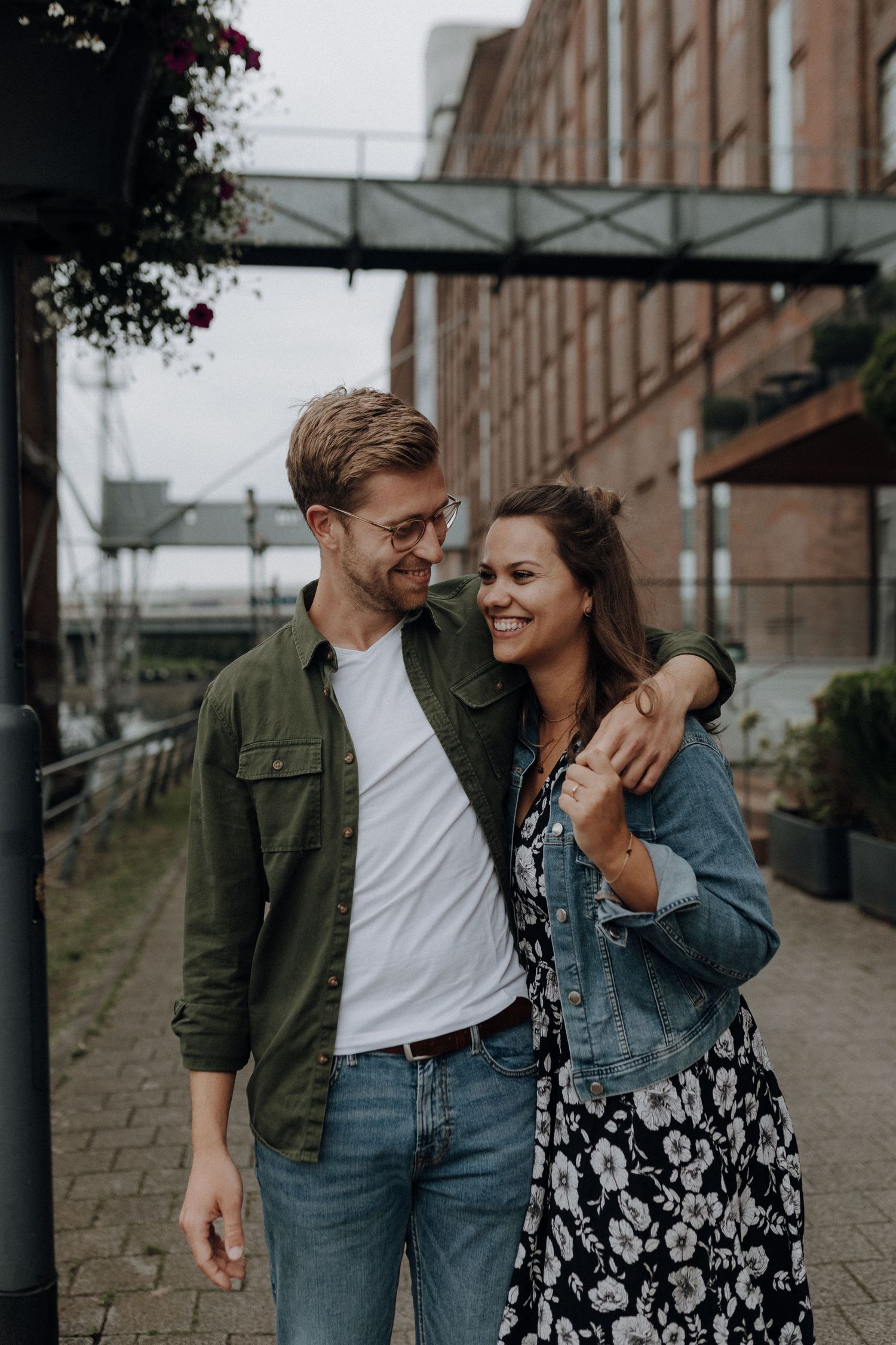 Happy couple embracing and smiling while walking together on a cobblestone street near a brick building.