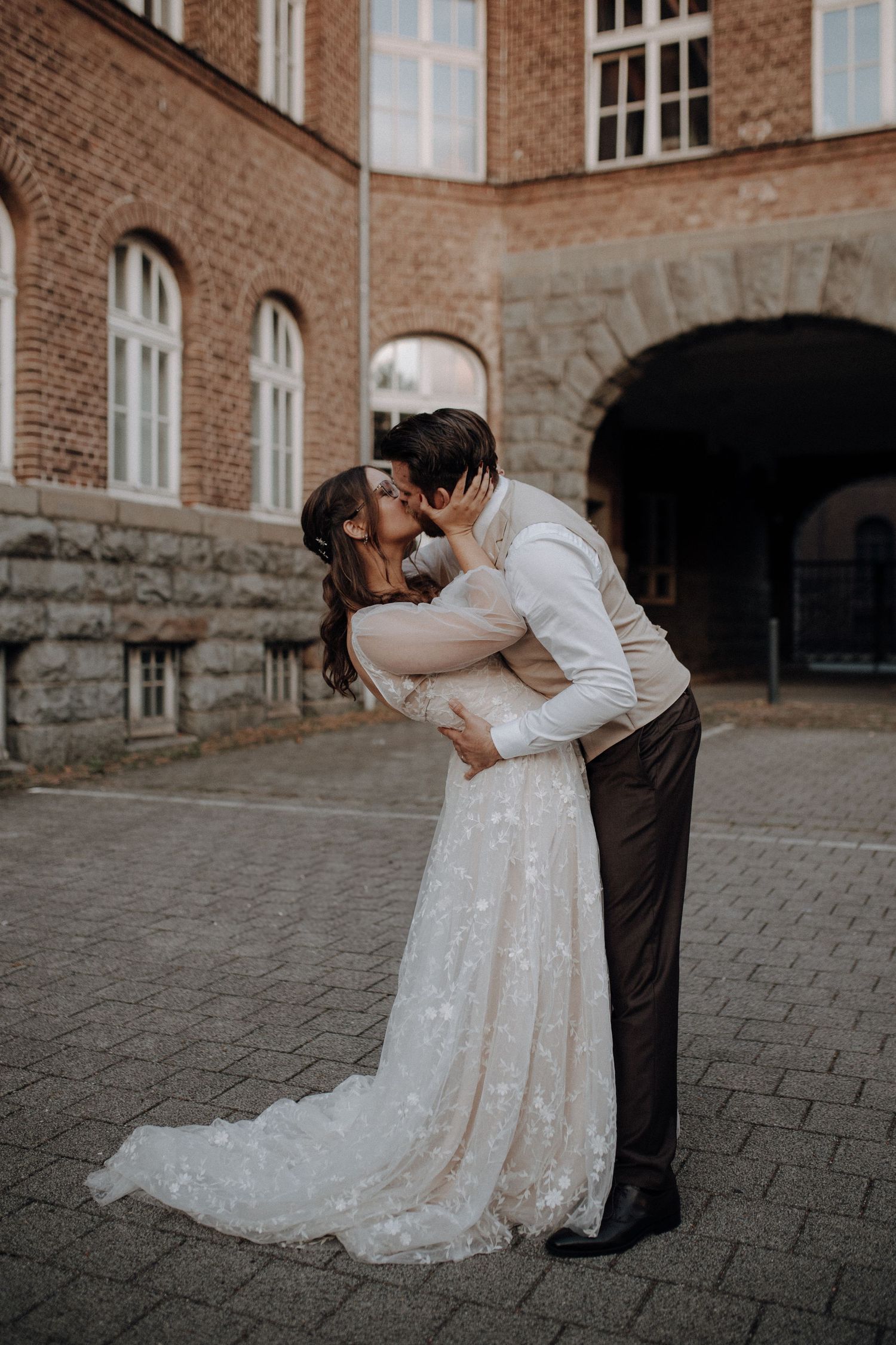 Bride and groom sharing a romantic kiss in front of a historic brick building on their wedding day.
