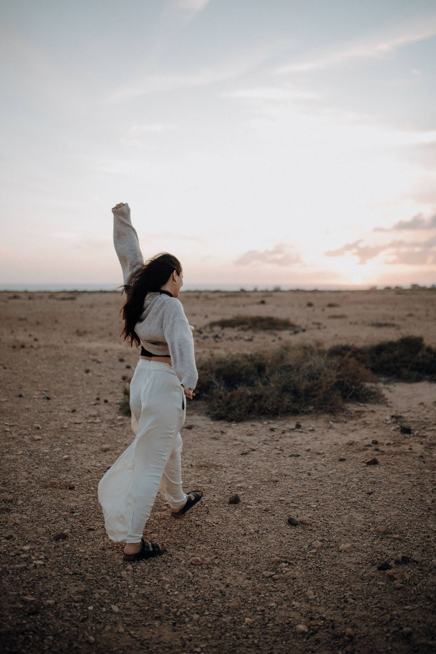 Woman in white outfit raising her fist at sunset in a vast desert landscape.