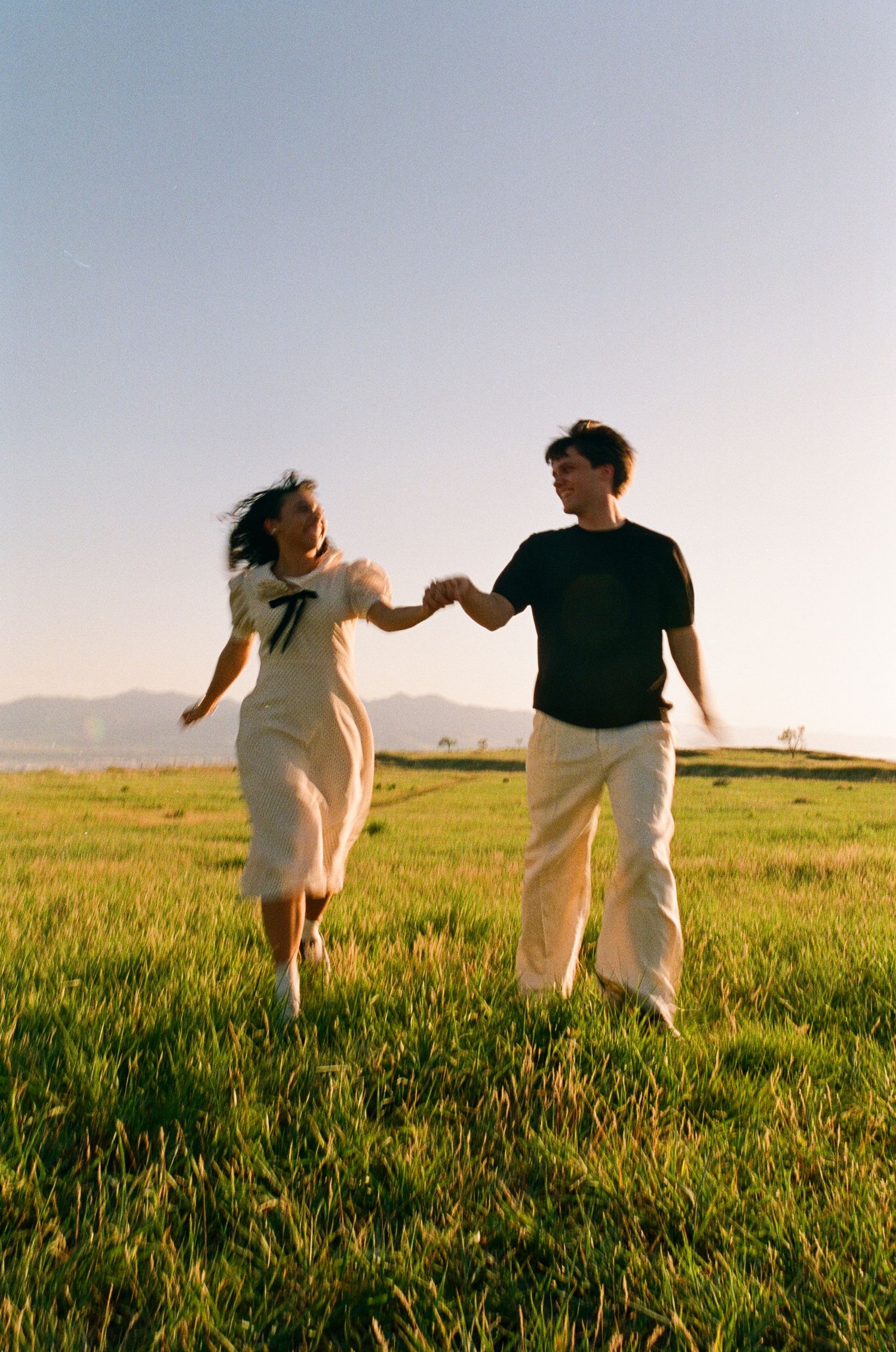 Candid 35mm film photo of a couple running hand in hand through a field in Utah.