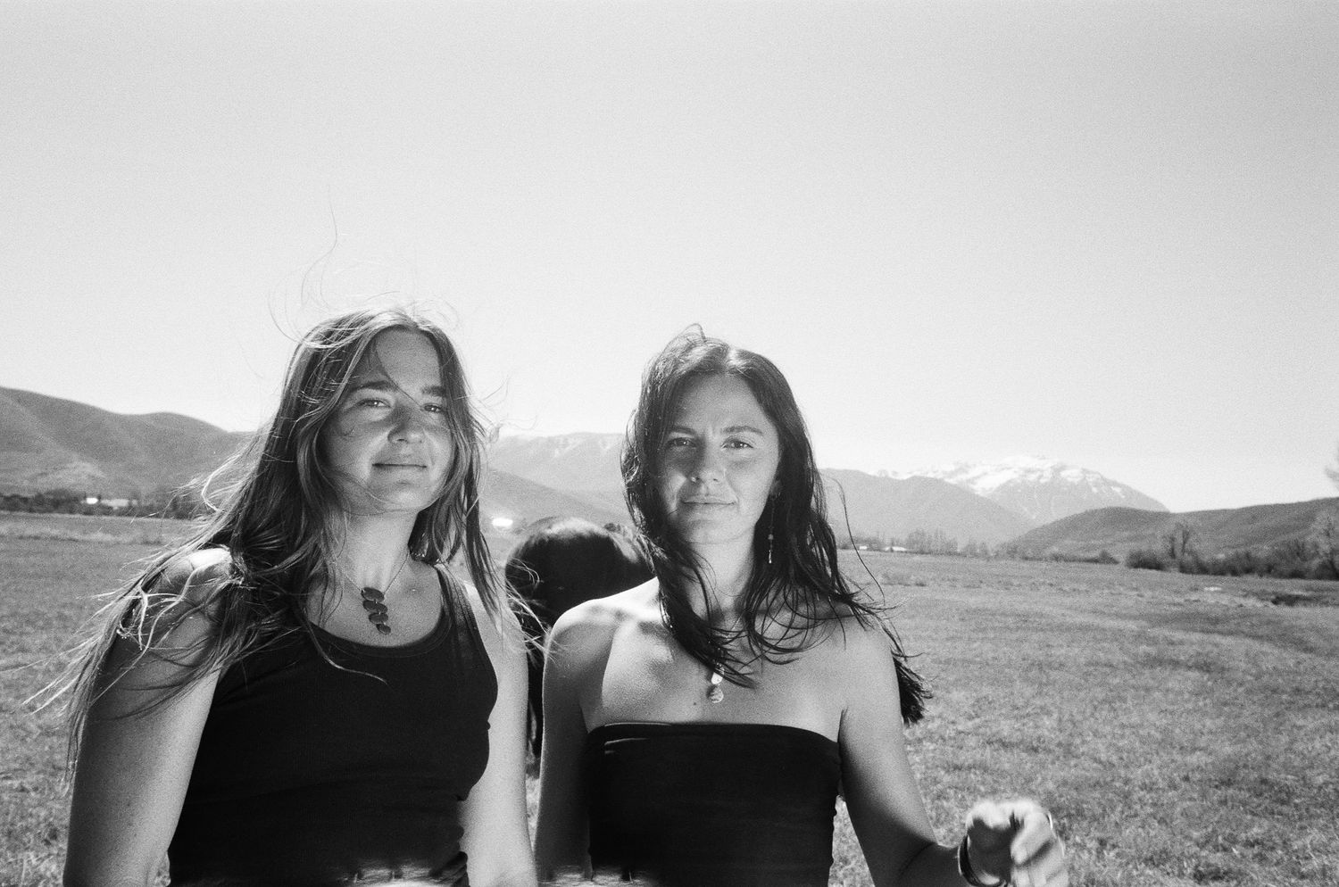 Black and white 35mm film portrait of two women in an open field with Utah mountains behind them.
