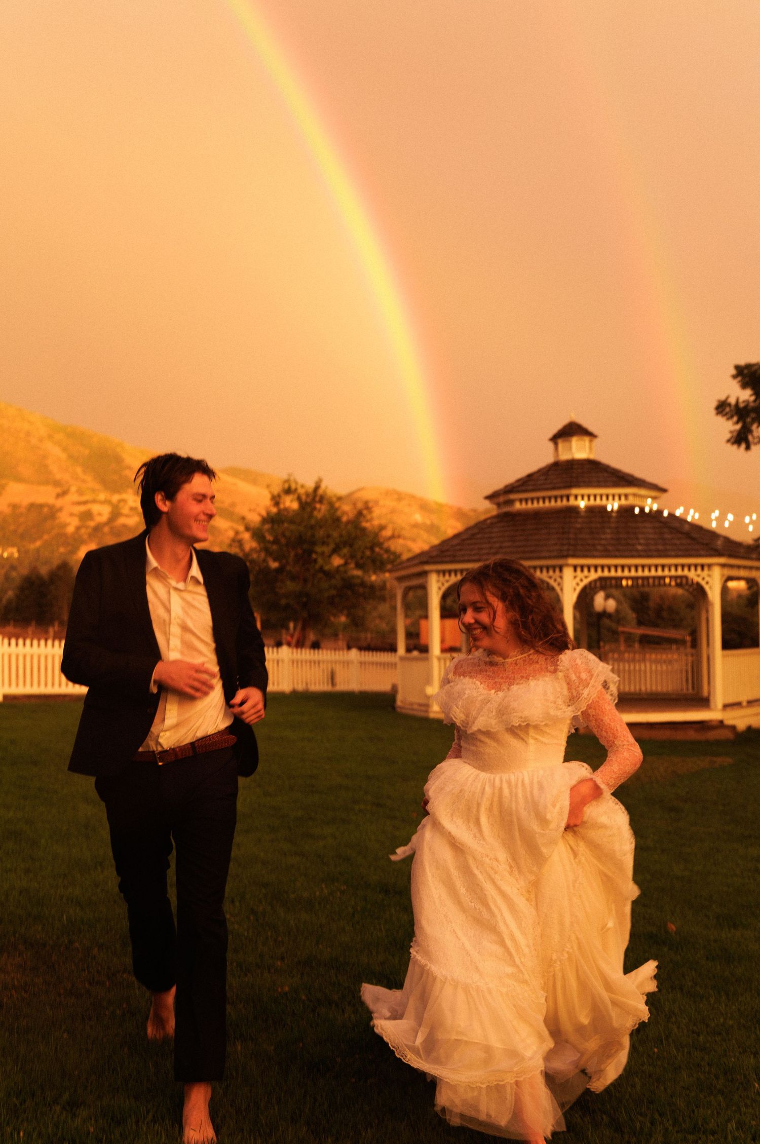 Bride and groom running beneath a rainbow at their Utah wedding.