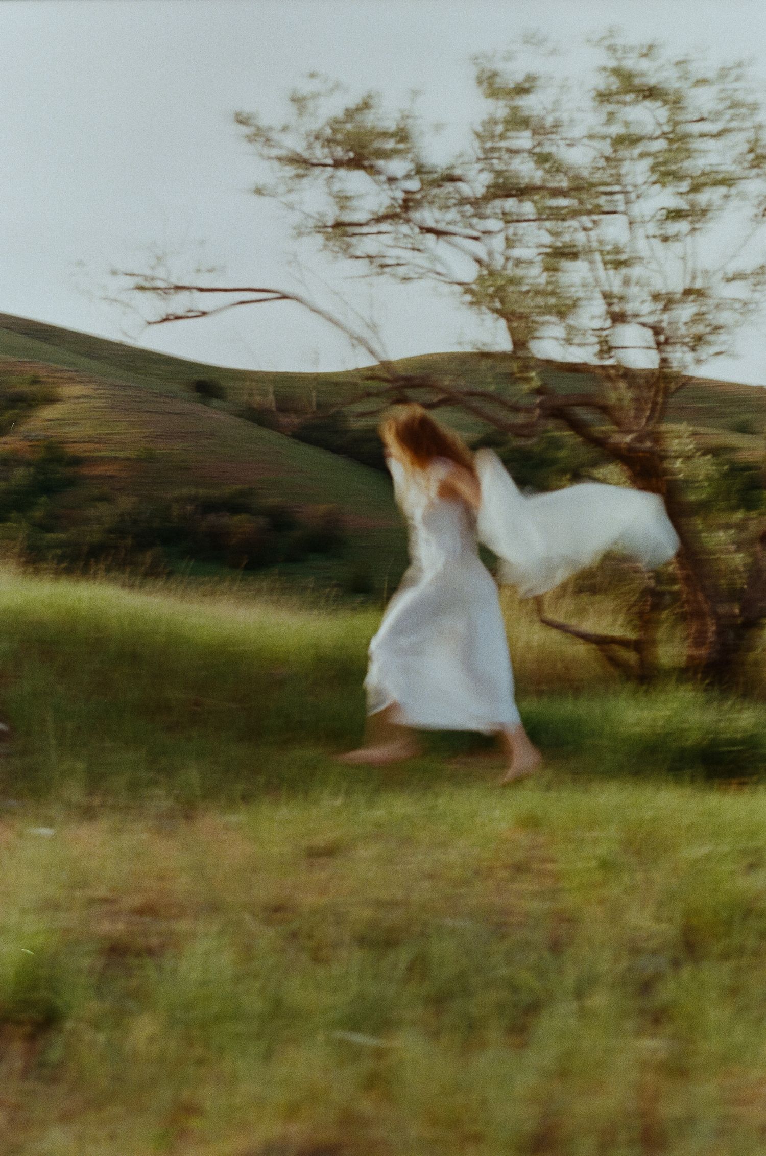 Dreamy 35mm film portrait of a woman running through a green field in the Utah mountains.