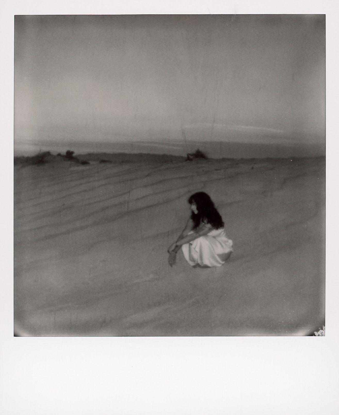 Black and white Polaroid portrait of a woman in an open desert landscape.