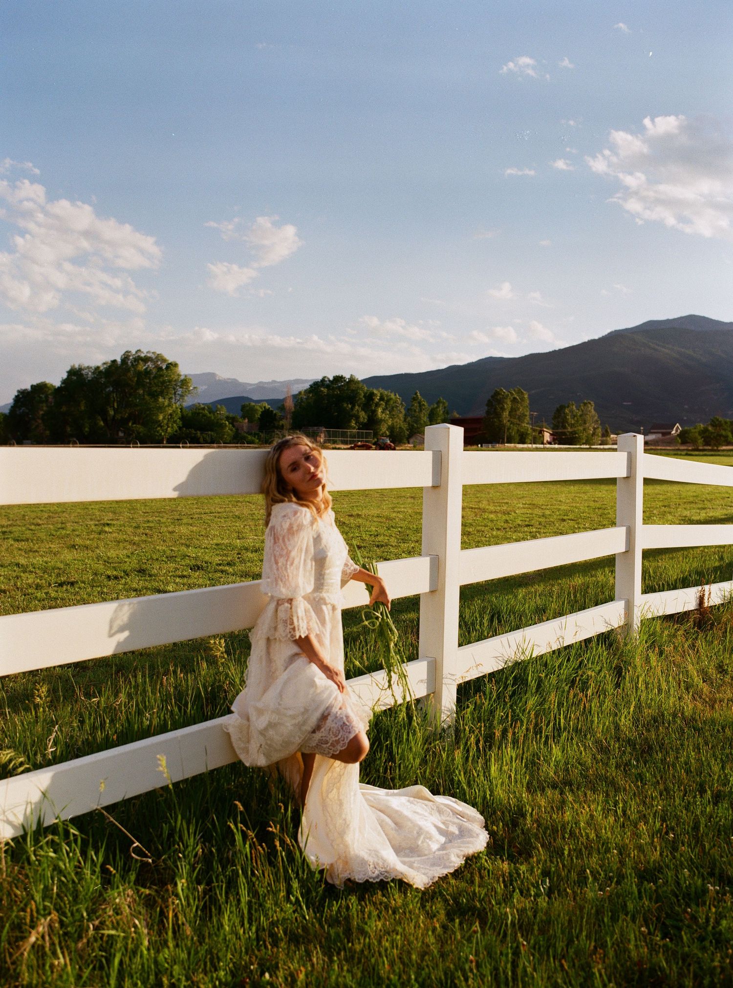 Medium format film bridal portrait beside a white fence in the Utah countryside.